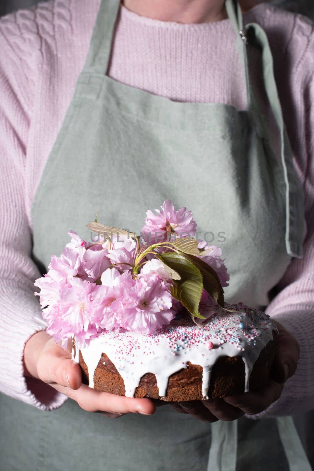 a woman decorates a homemade Easter cake with pink sakura flowers,spring blossom by KaterinaDalemans