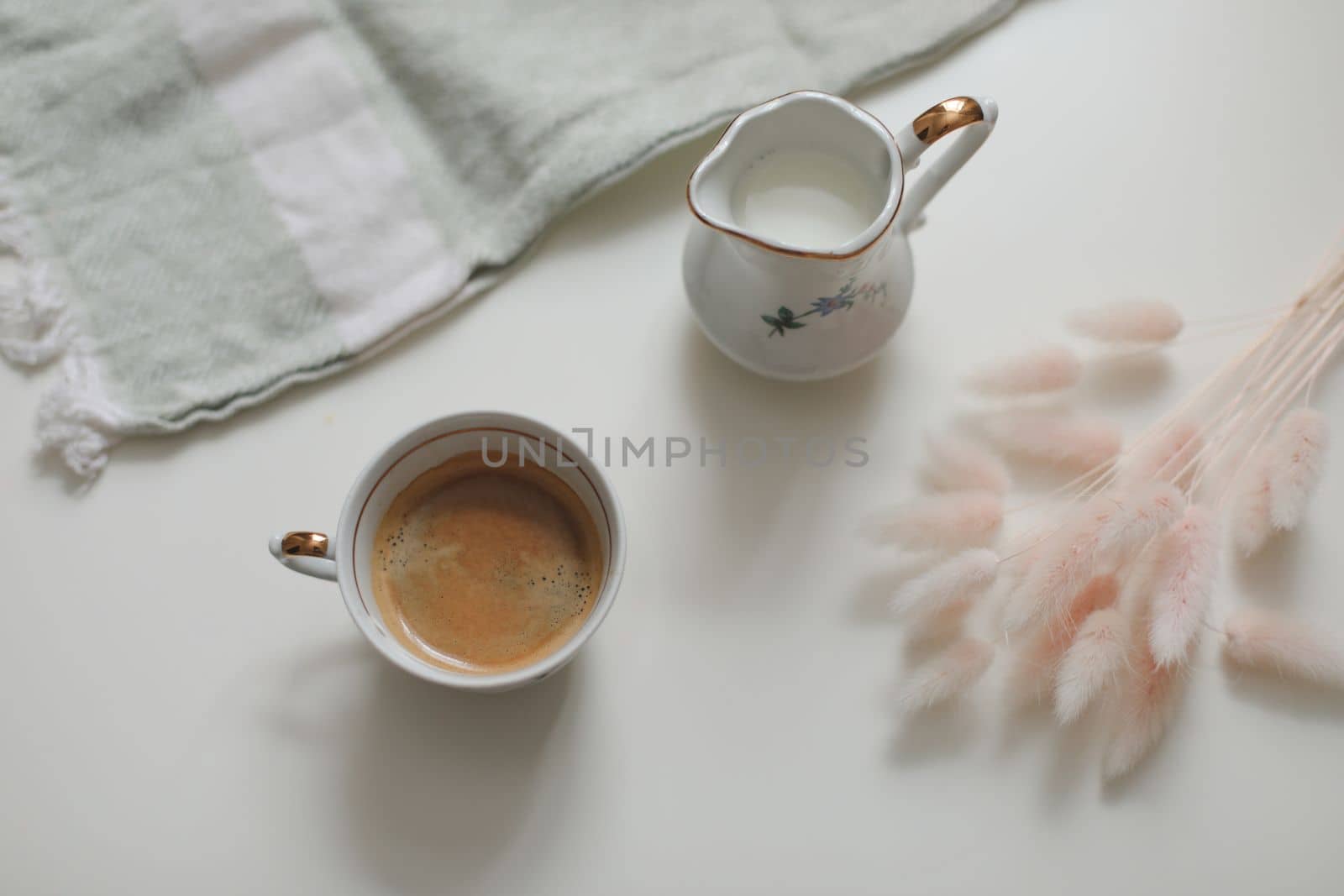 White cup with coffee and milk jug on a white wooden background, closeup. Energy breakfast, morning routine concept. coffee cup and milk pitcher on white table background
