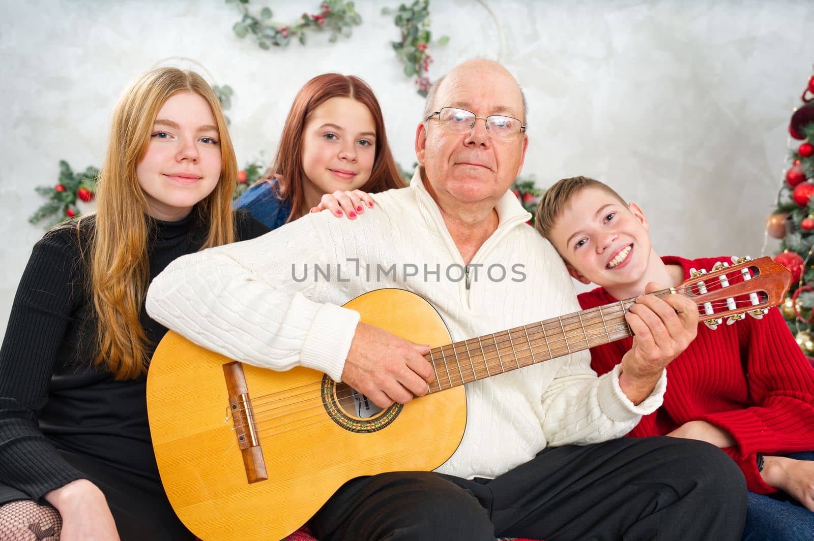 Grandfather playing guitar during christmas for grandchildren. Happy man 60s playing guitar christmas songs. by PhotoTime