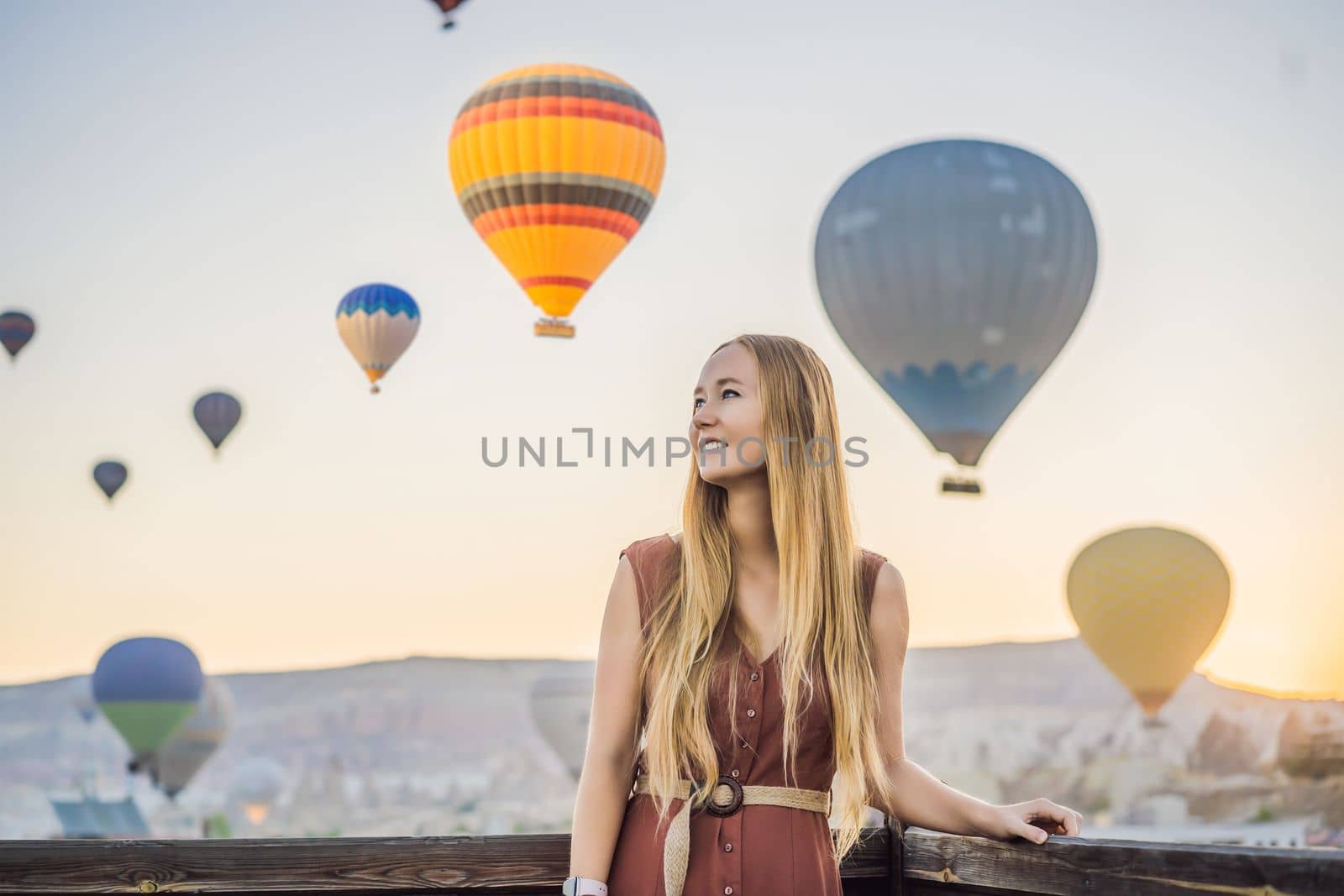 Tourist woman looking at hot air balloons in Cappadocia, Turkey. Happy Travel in Turkey concept. Woman on a mountain top enjoying wonderful view.