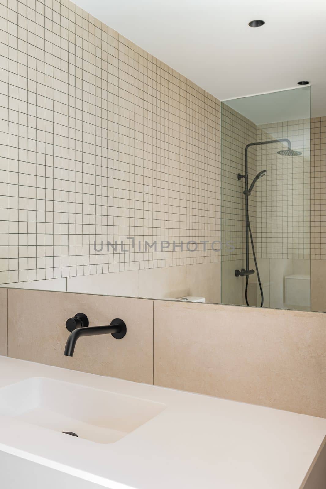 Modern bathroom with beige tiles, white sink and black faucet. Shower zone with glass partition reflected in the mirror.