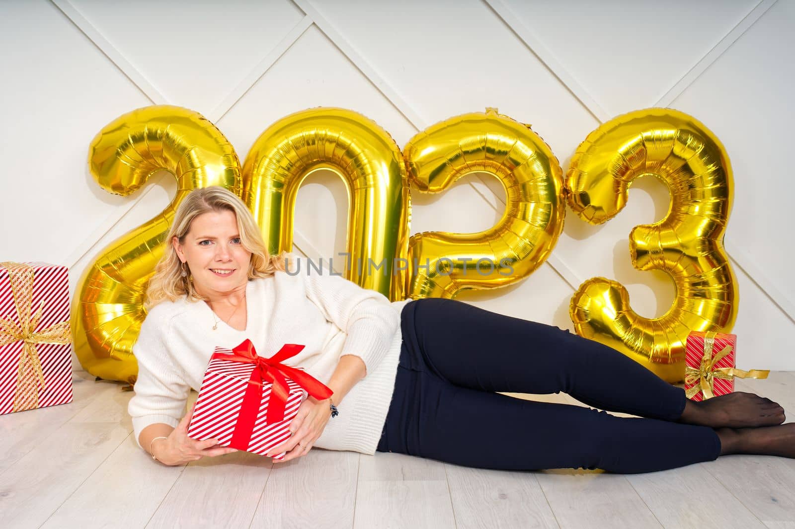 beautiful woman lies in front of the numbers from golden foil inflatable balloons 2023 on Christmas eve. by PhotoTime