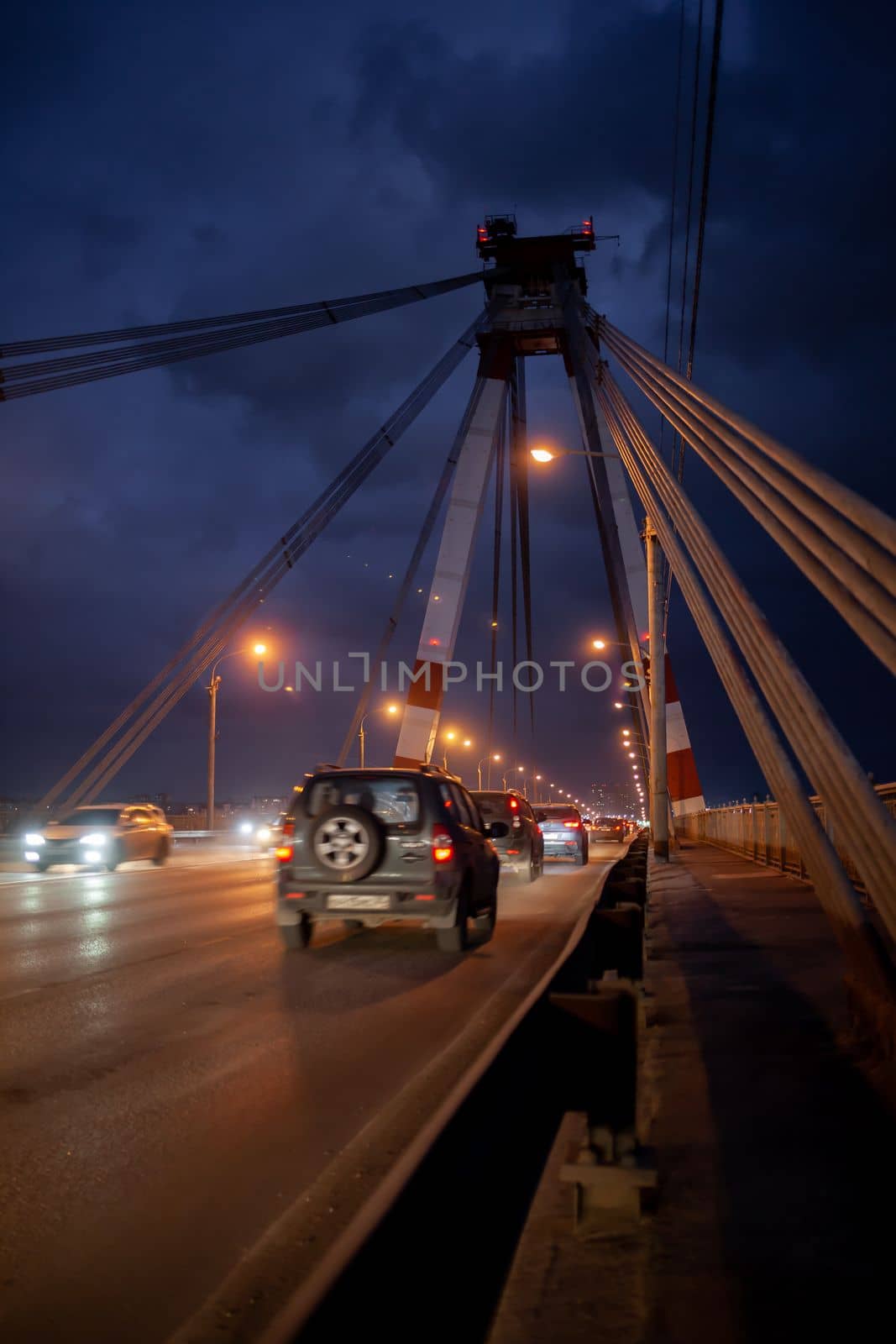 A large automobile bridge on which cars drive at night.  by AnatoliiFoto