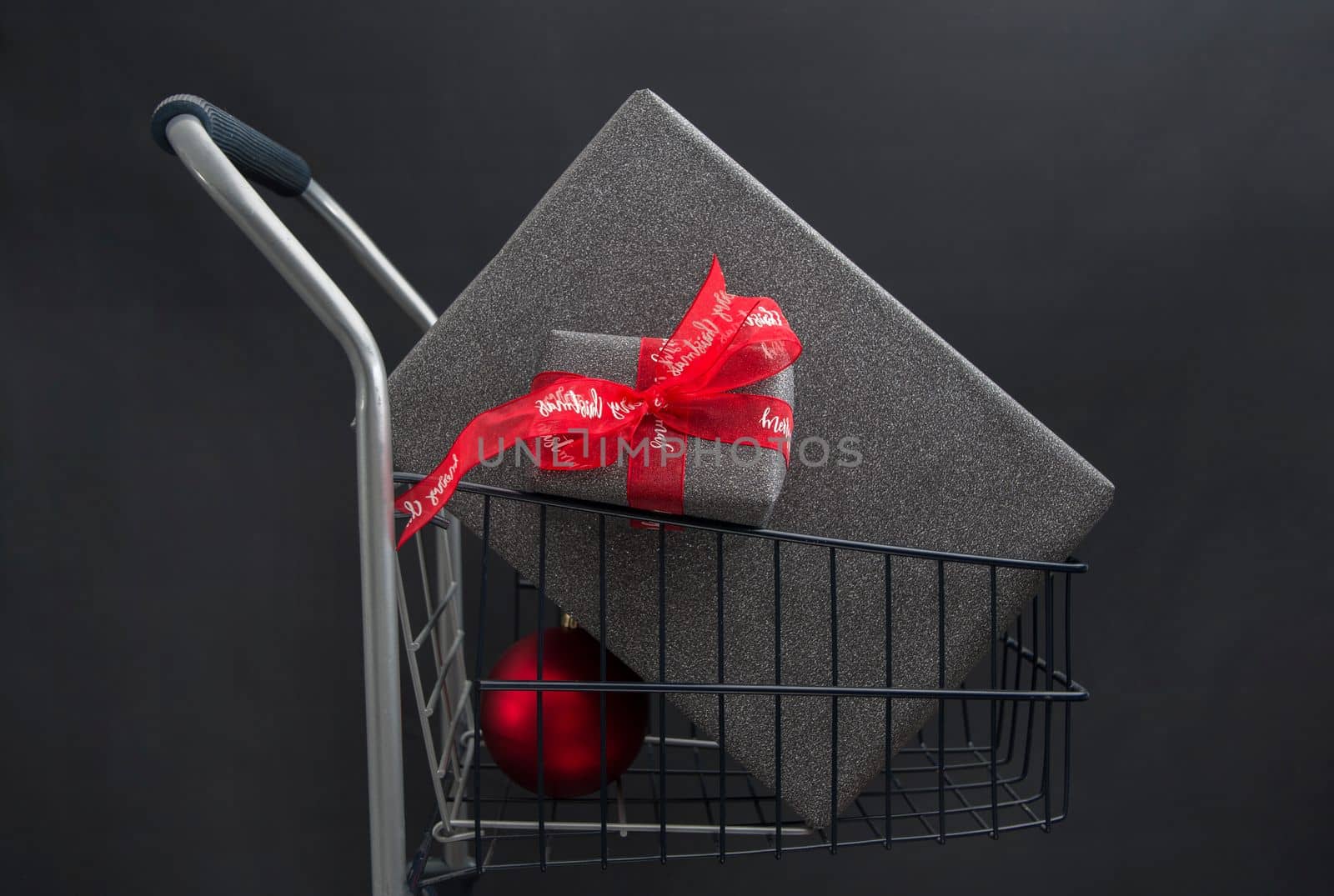 Christmas gift boxes in black paper in a shopping basket with red balls on a black background. High quality photo