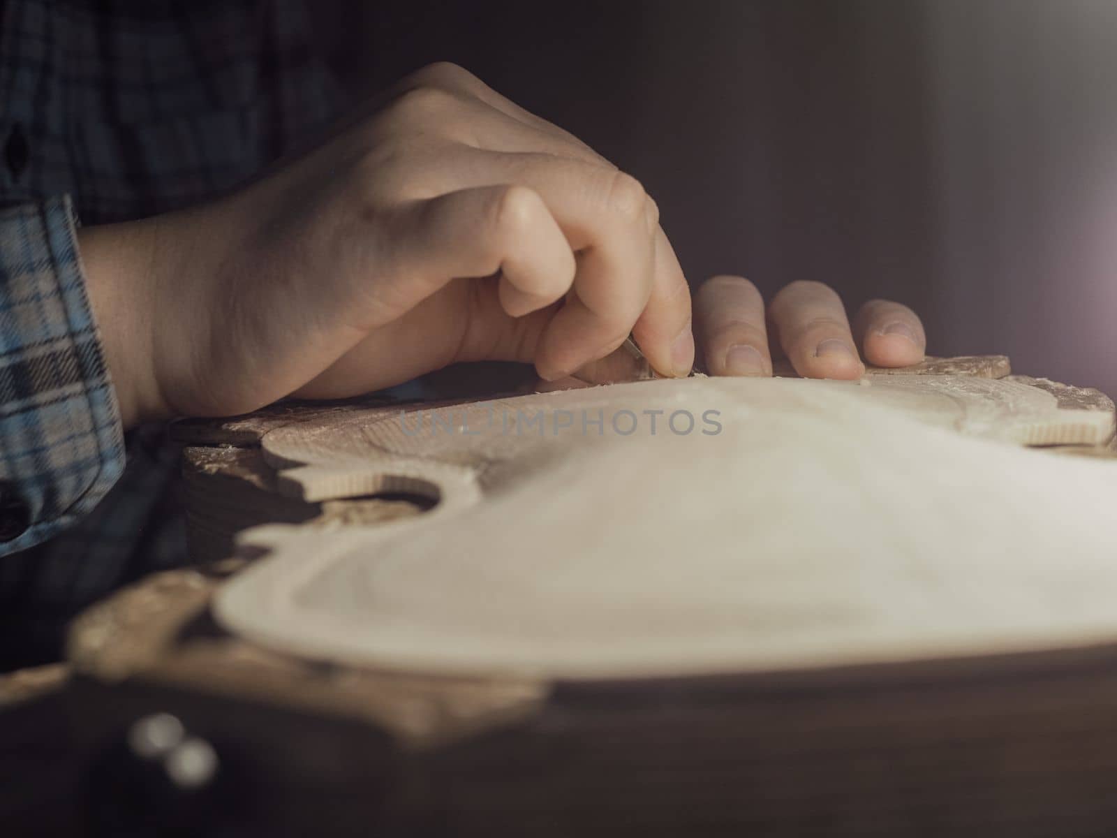 artisan working on raw wood violin plate with finger plane on the bench