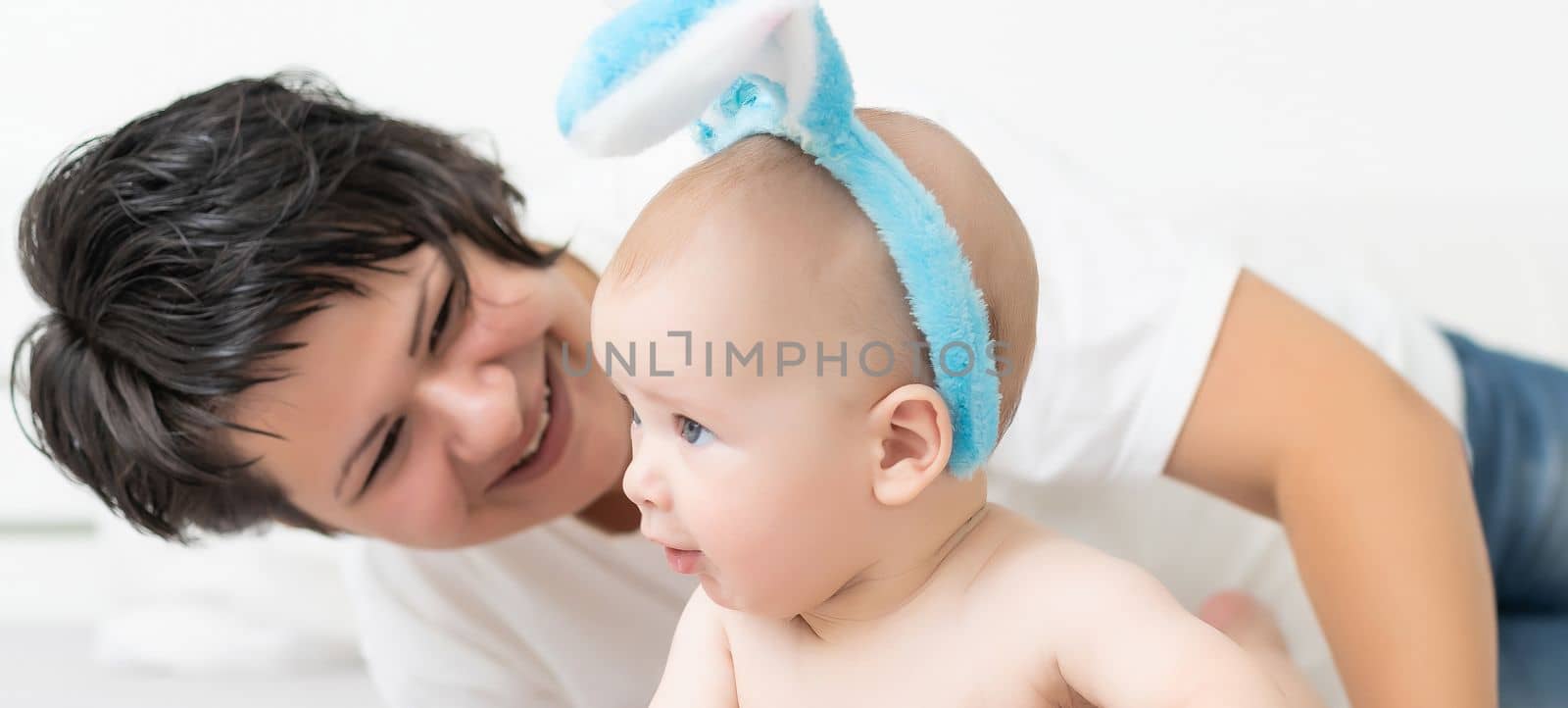 Mother and child with colorful eggs. Mom and baby with bunny ears. Parent and kid play indoors in spring. Family celebrating Easter.