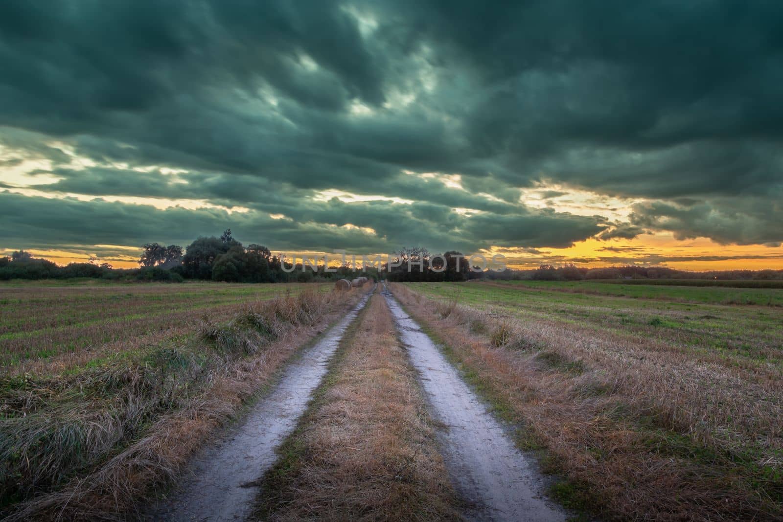 Dirt road through the fields and cloudy sky, September view in eastern Poland