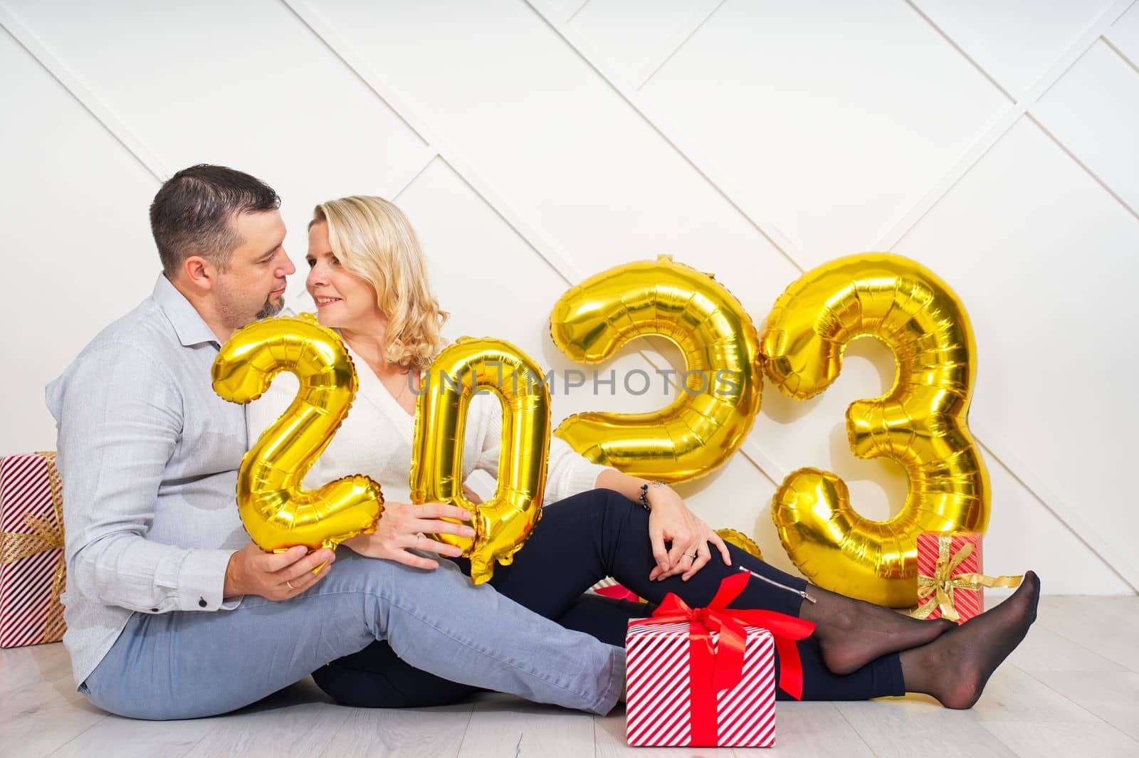 Young couple having romantic date on Christmas eve with 2023 golden foil inflatable balloons. by PhotoTime