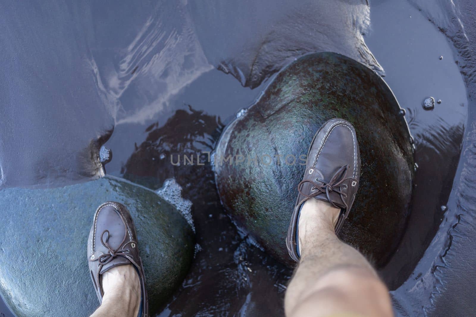 male feet in top siders on green stones over water by Chechotkin