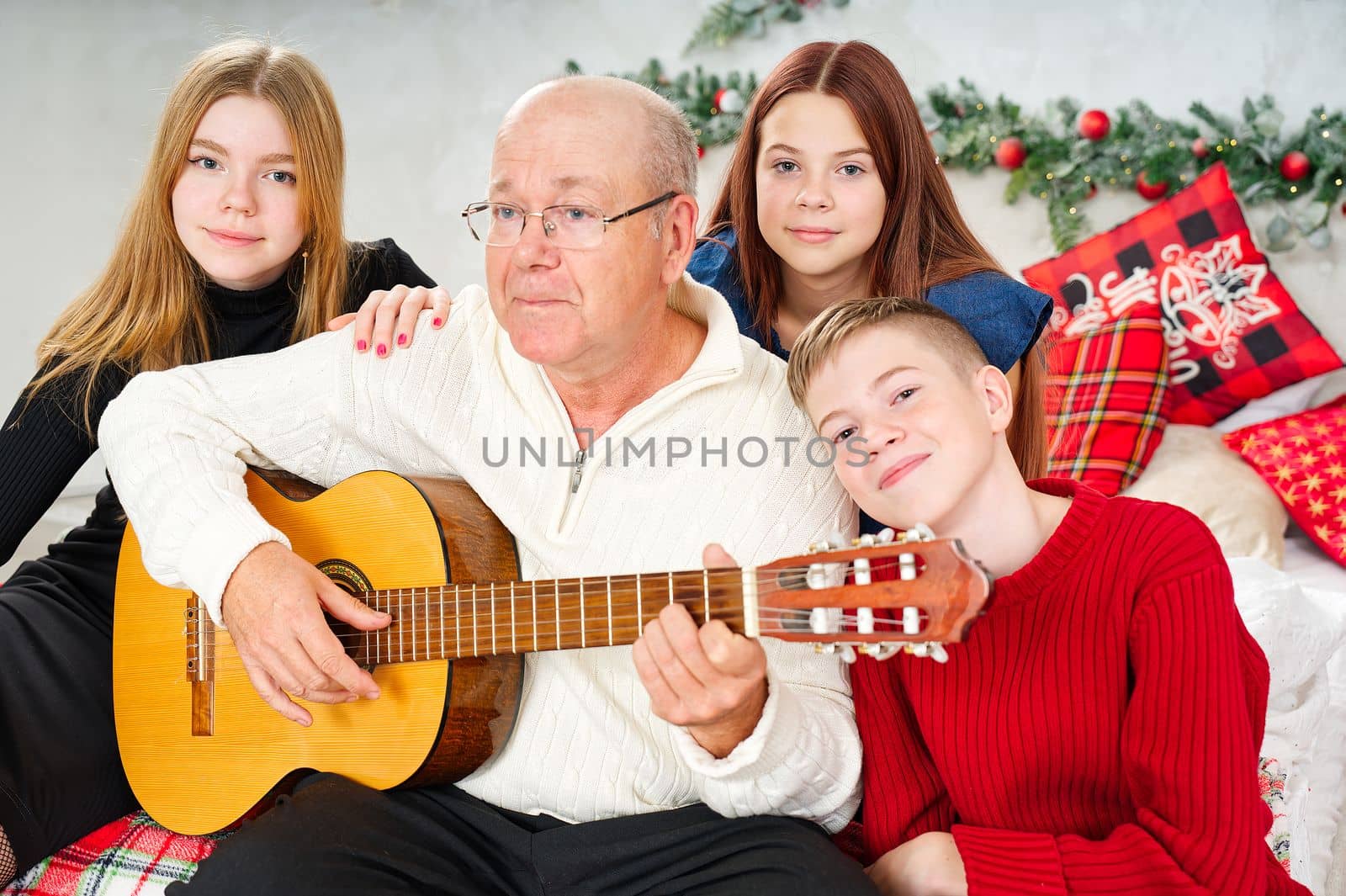 Grandfather playing guitar during christmas for grandchildren. Happy man 60s playing guitar christmas songs. by PhotoTime