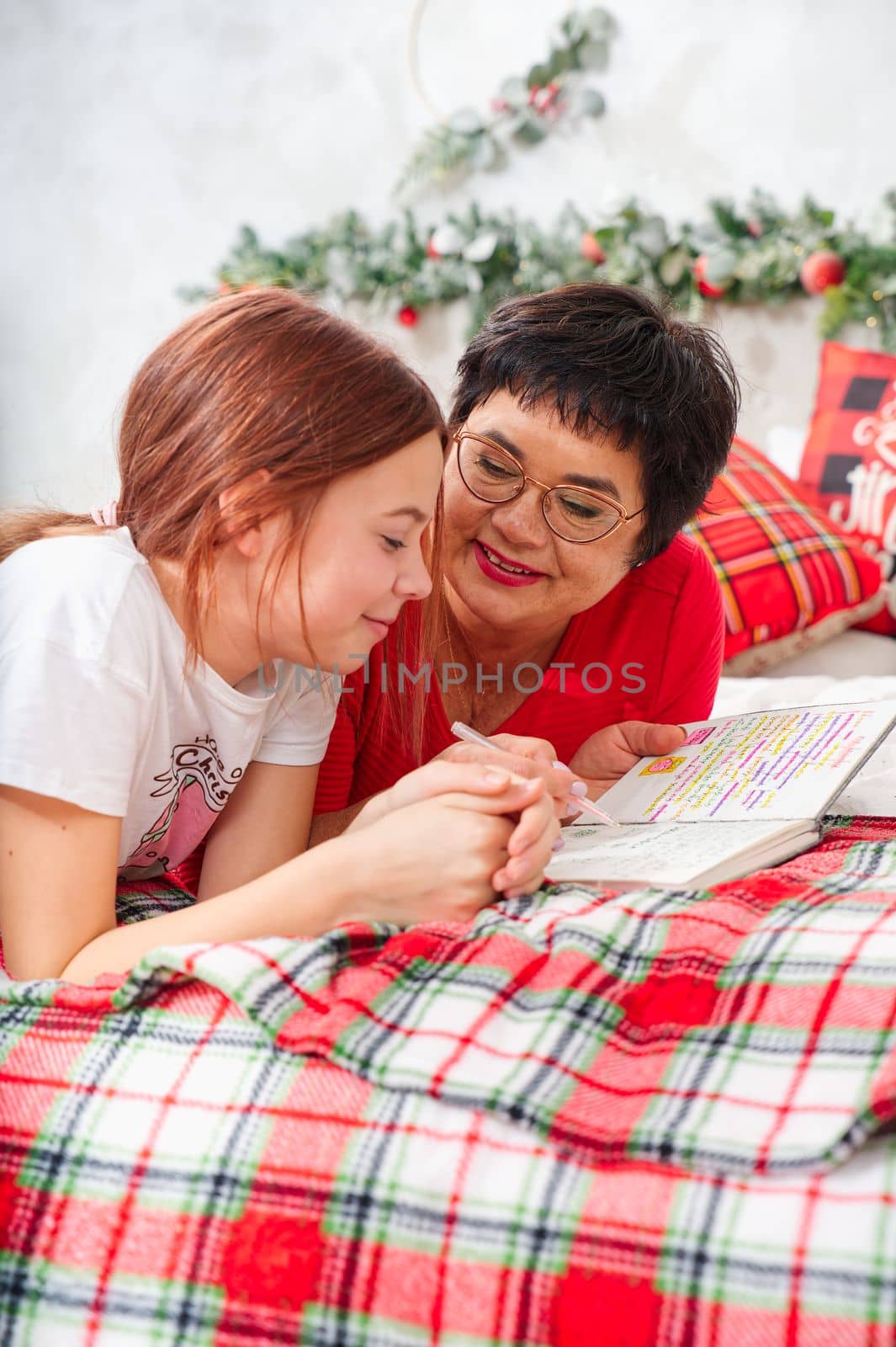 happy mother with daughter with pen and notebook making wish list or to do list for new year in bed over christmas tree. xmas holidays concept by PhotoTime