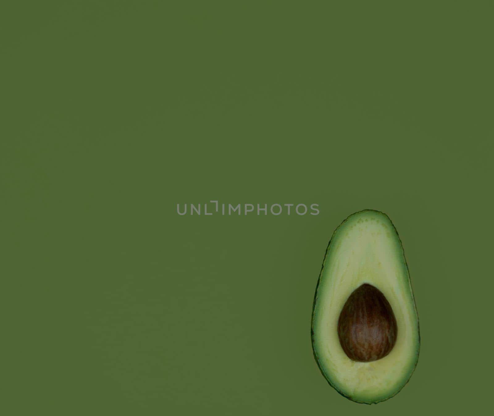 Avocado fruit half on green background. Green avocado, minimal flat lay style with copy space. High quality photo