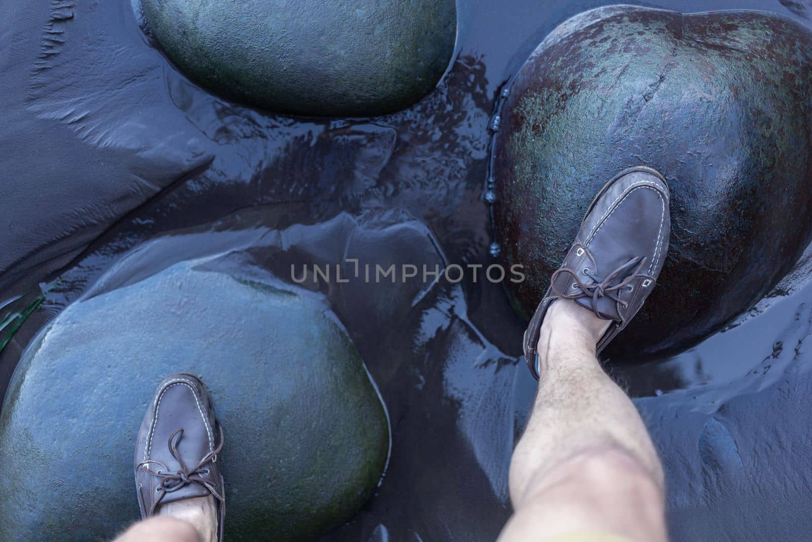 male feet in top siders on green stones over water by Chechotkin