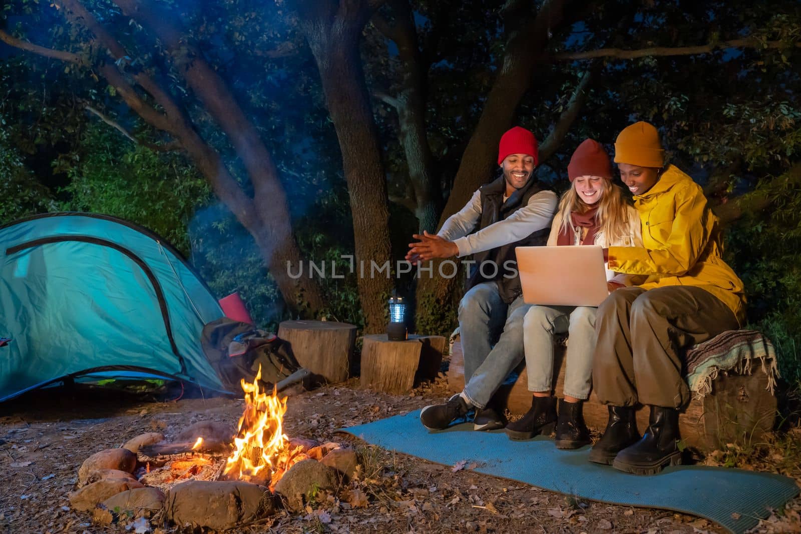 Happy multiethnic friends having fun playing music and enjoying bonfire camping in nature at night by PaulCarr