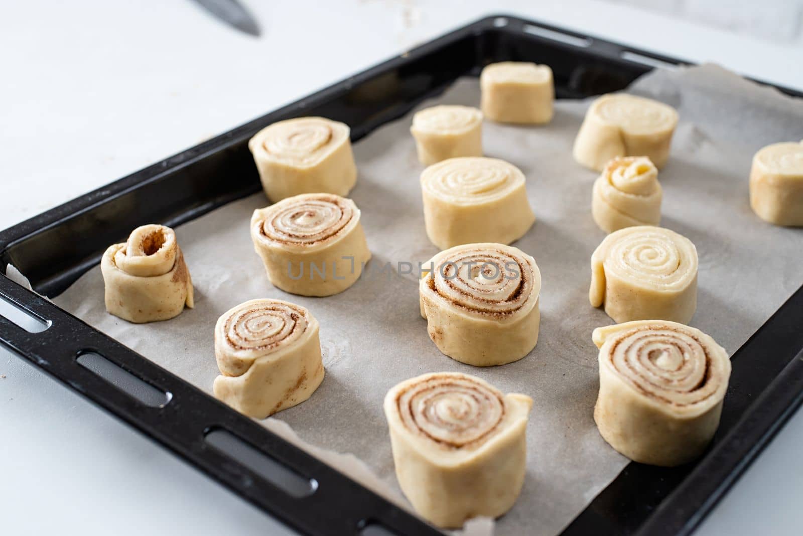 freshly made cinnamon rolls on the baking tray, christmas tree with lights on the background, festive cooking