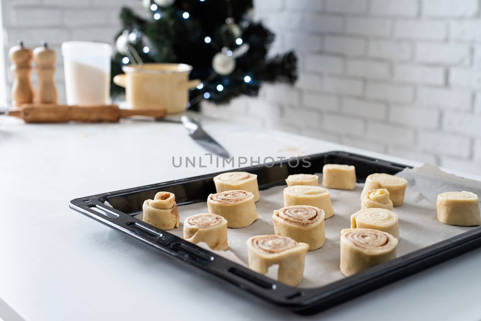 freshly made cinnamon rolls on the baking tray, christmas tree with lights on the background, festive cooking