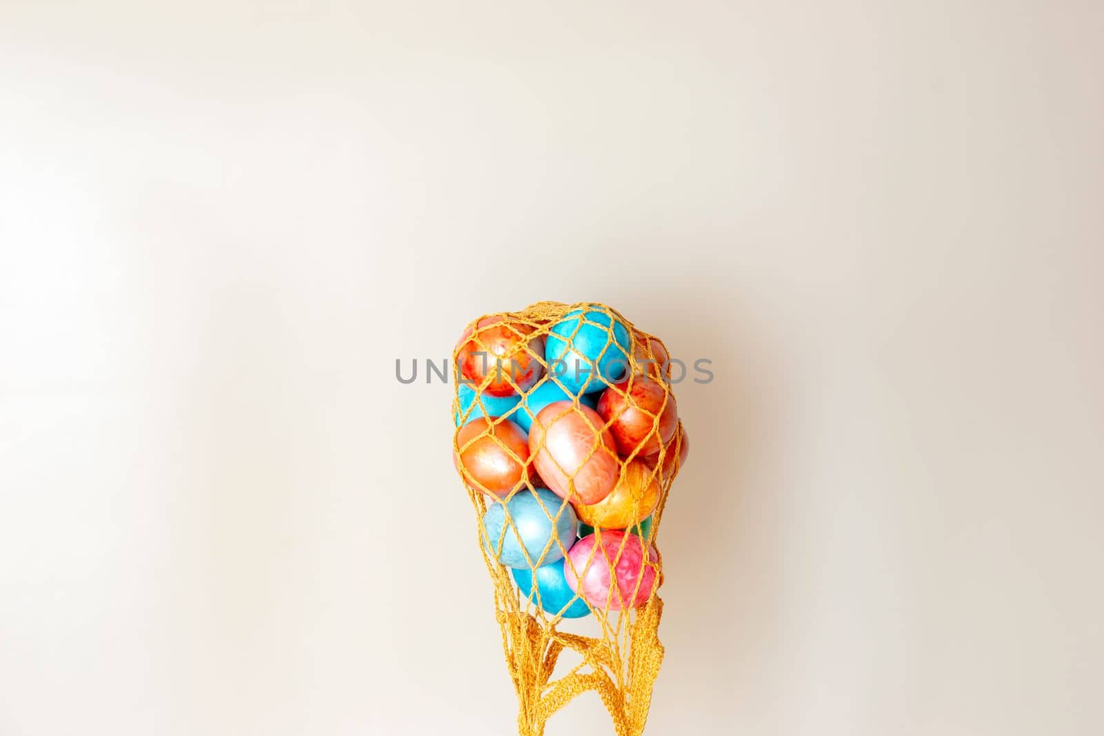 A funny, creative photo, several colorful eggs in an inverted gold knitted bag, against a beige background. Copy space