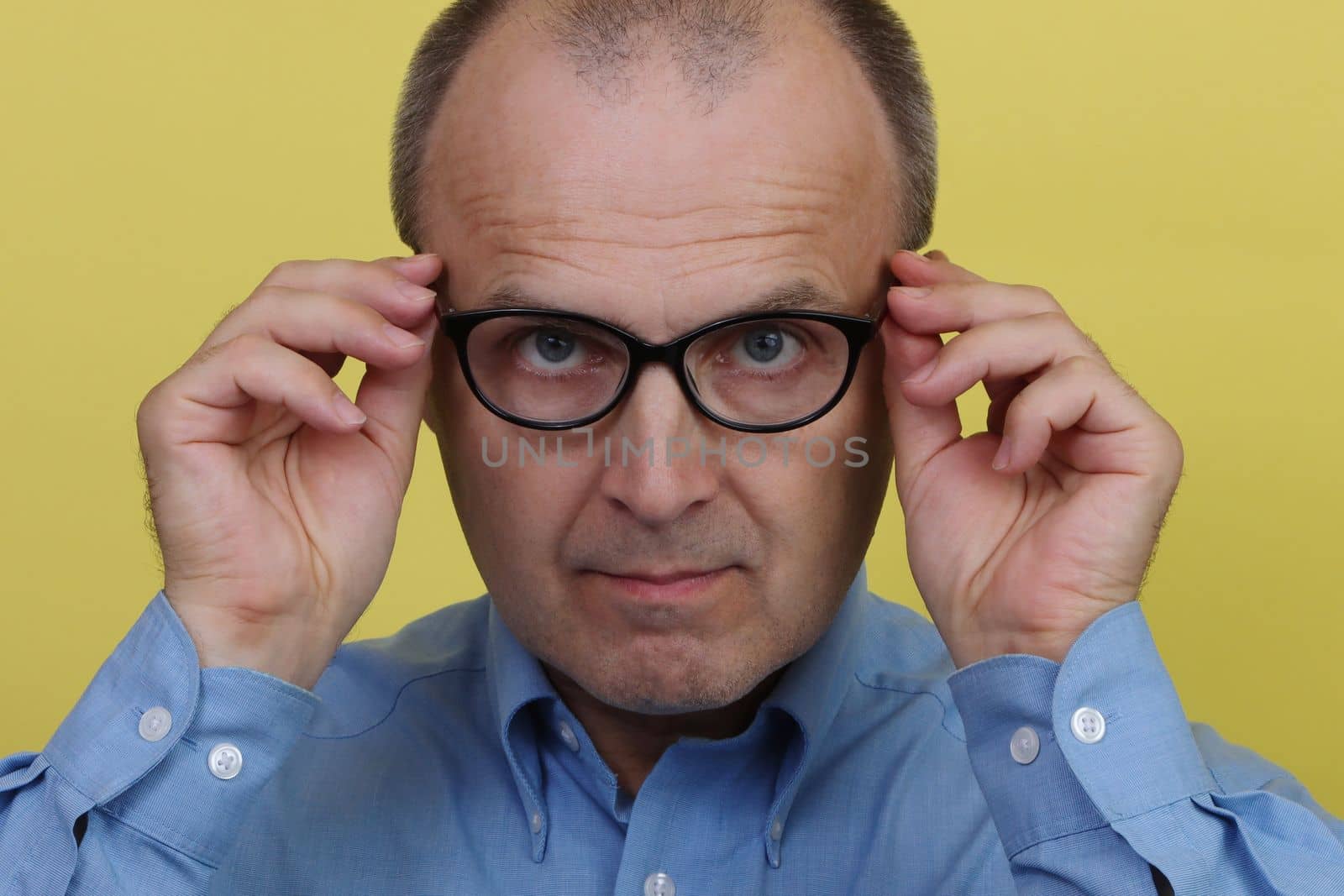 Man in blue shirt on yellow background holding transparent glasses.
