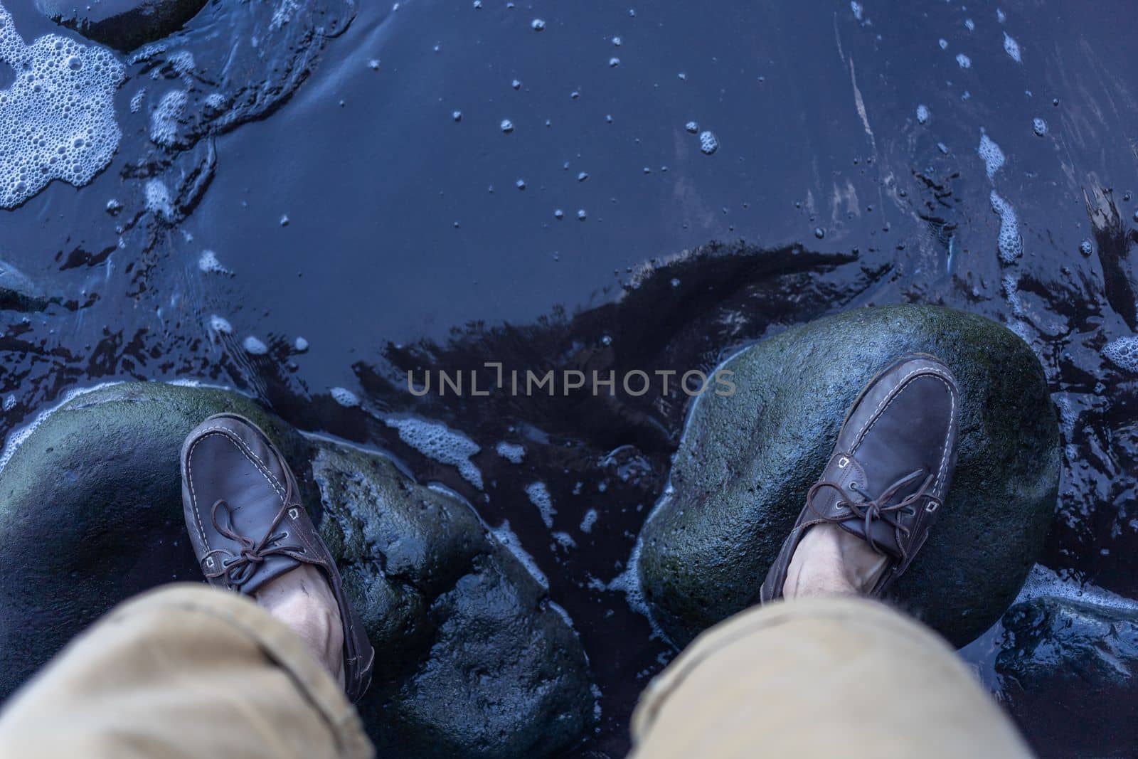 male feet in top siders on green stones over water by Chechotkin
