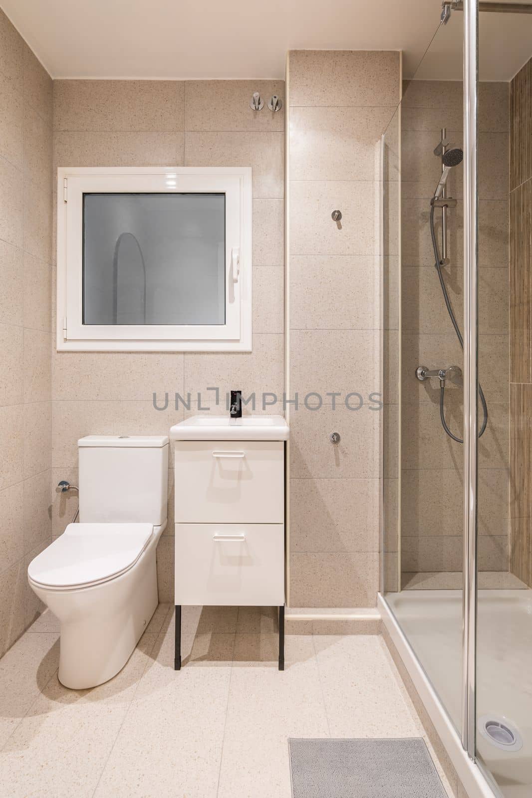 Bathroom with small shower area enclosed by transparent glass wall. Washbasin on furniture with drawers for bathroom accessories. Window in wall with frosted glass and white frame