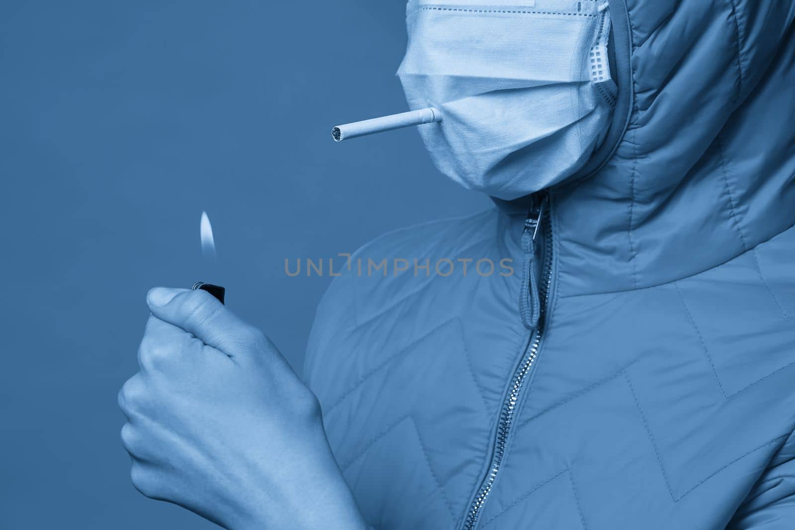Young girl wearing medical protective mask lights up, holding a cigarette in her mouth through the mask by Mariakray