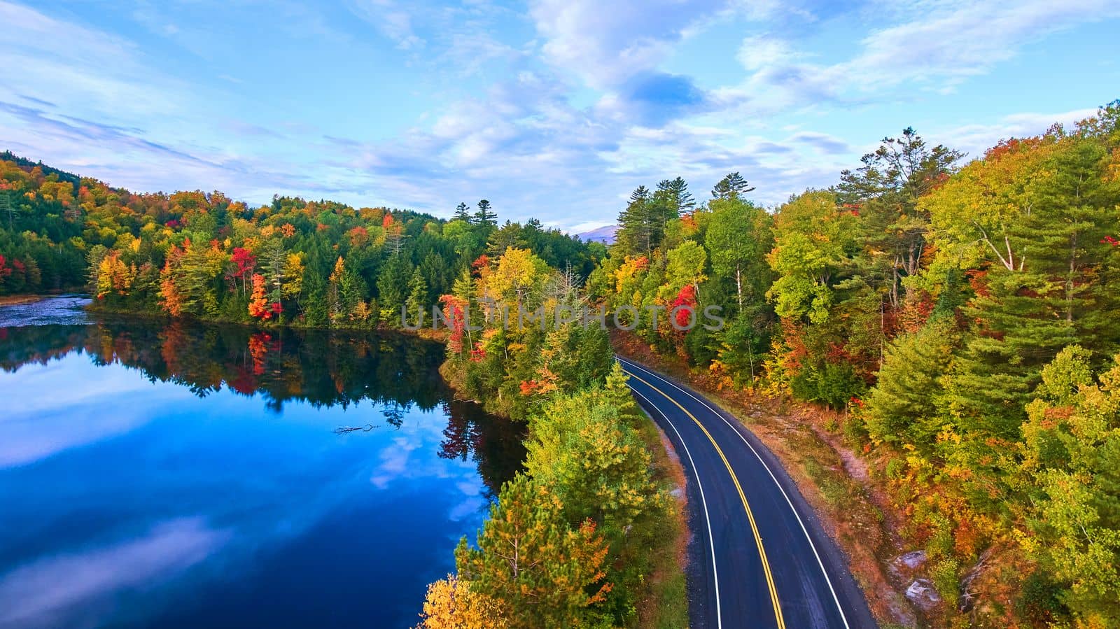 Image of Aerial over road next to blue lake and surrounded by fall forest