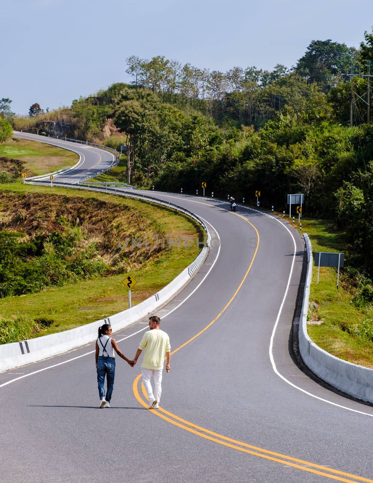 A couple walking at a curved road in the mountains of Nan Thailand, Road nr 3 country road  by fokkebok