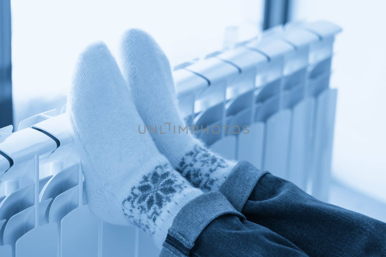 Woman warming up with feet on heater wearing woolen socks by Mariakray