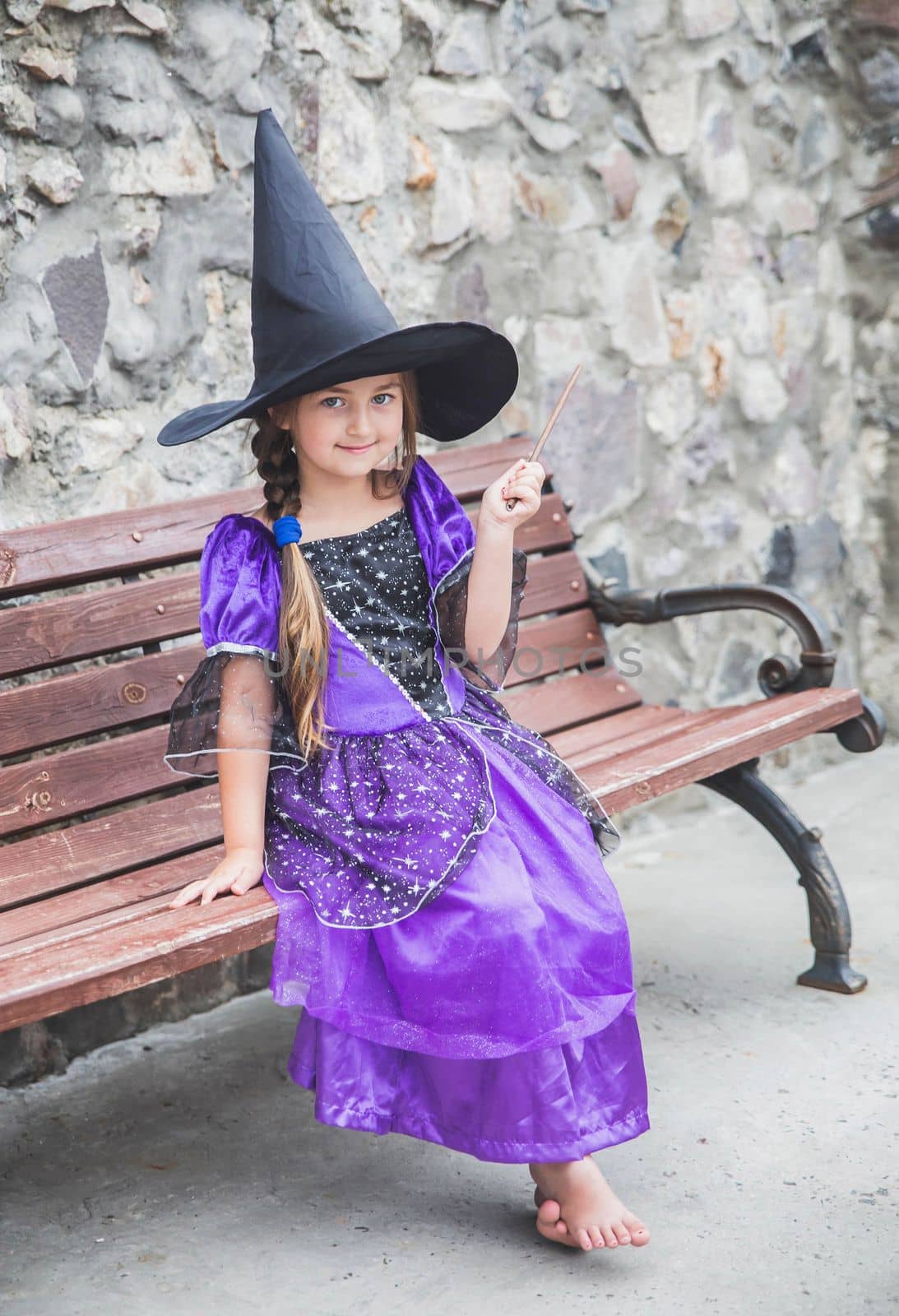 charming young sorceress sitting with a magic wand on a bench.