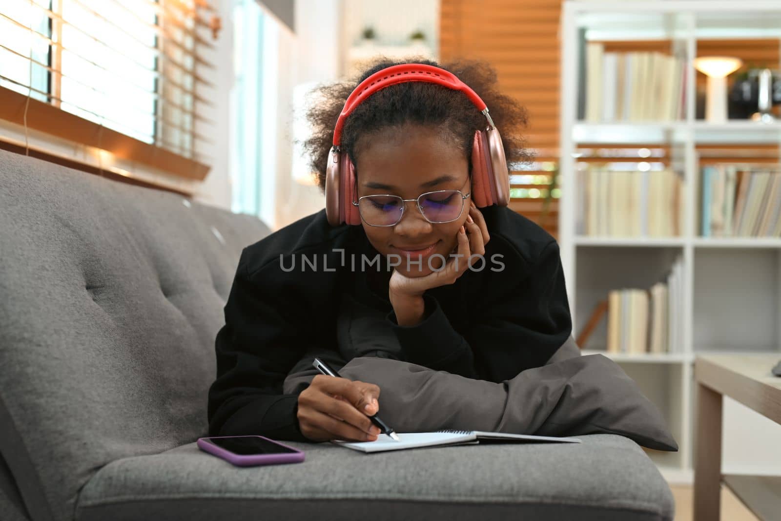 Pleasant young woman wearing headphone and writing records to daily planner on notebook.