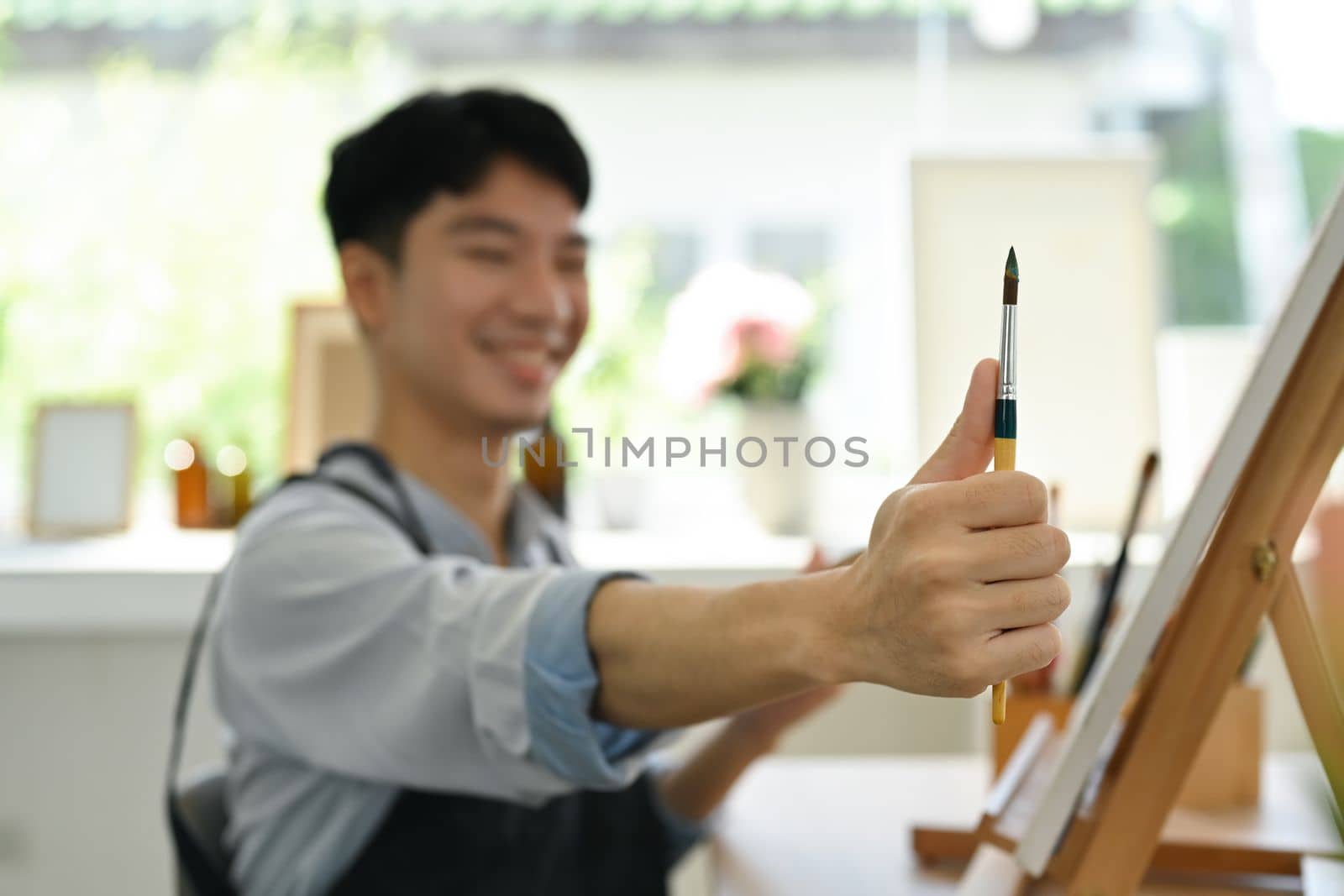 Image of pleased man artist painting picture with watercolor on canvas in art workshop. Art, creative hobby and leisure activity concept.