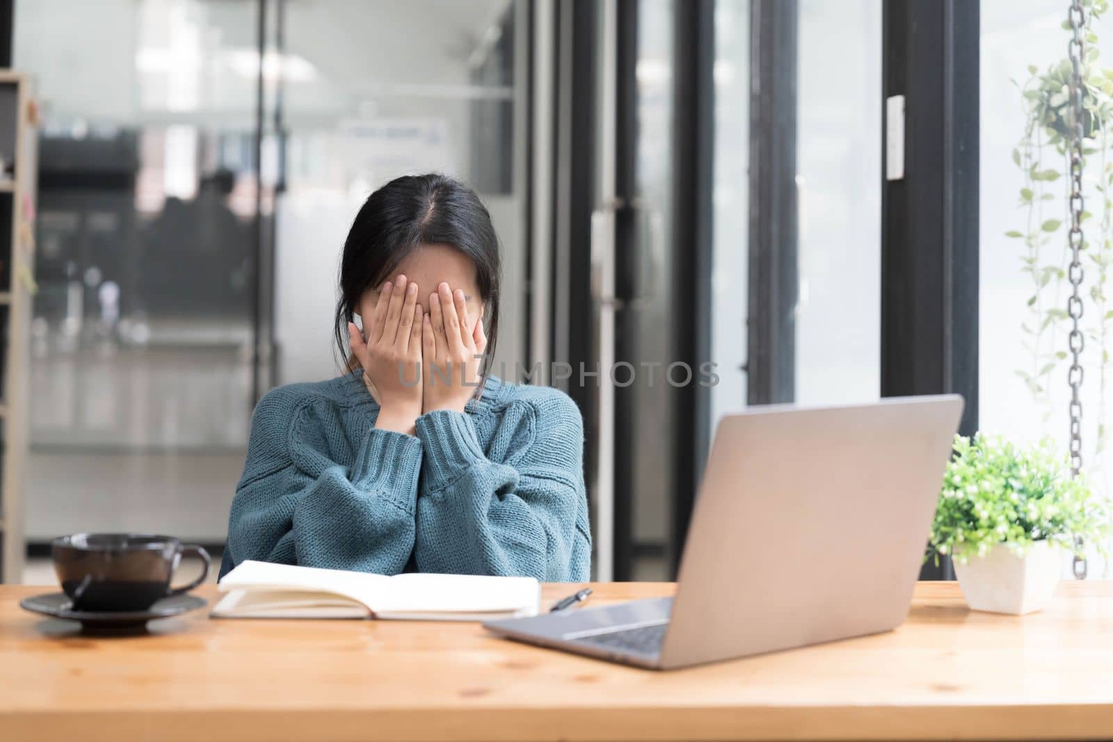 Young woman looks stressed, sitting at the desk, using a laptop, thinking and looking at the camera, feeling tired and bored with depression problems.