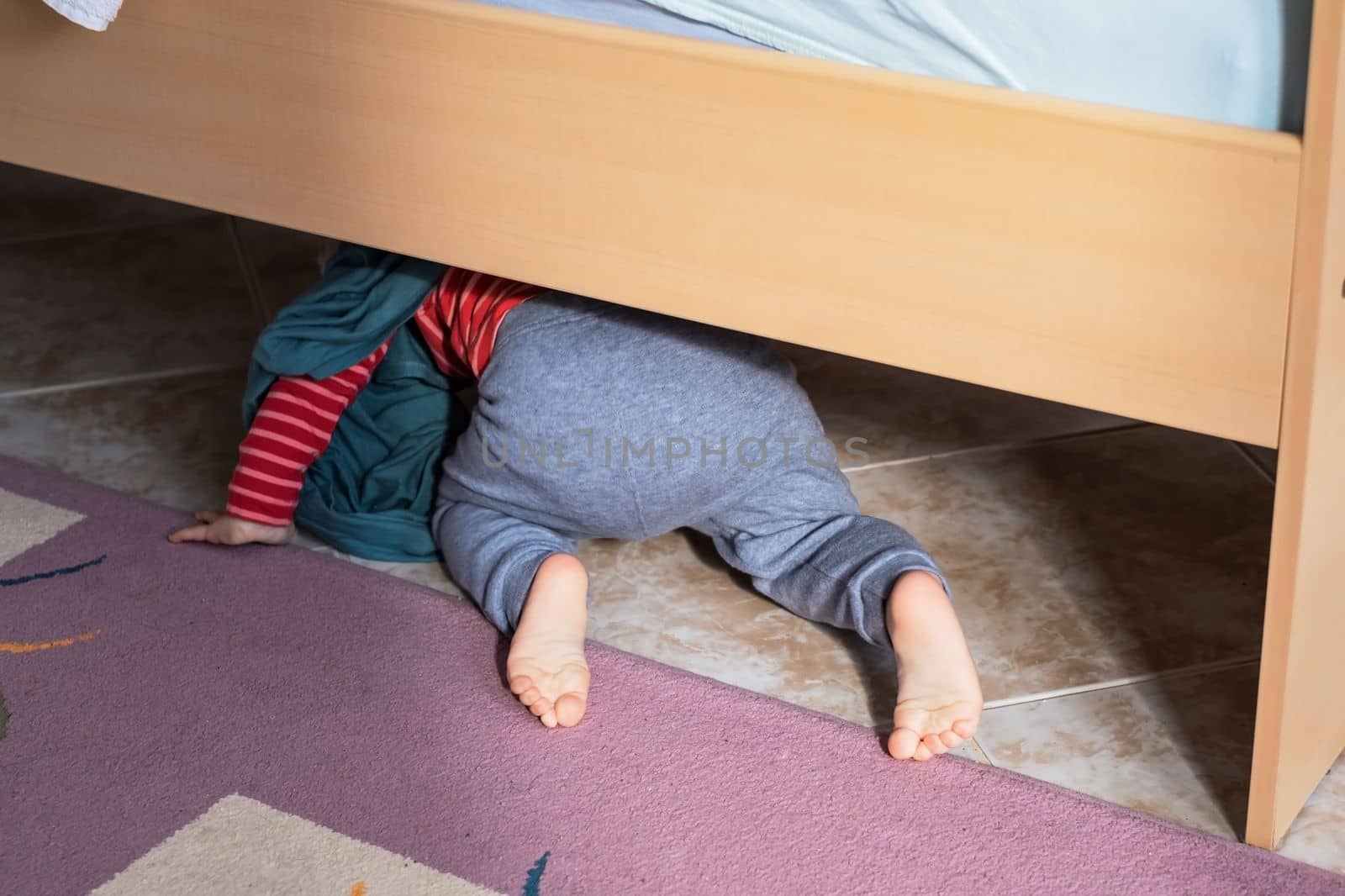 View on the bed on cute baby crawling on floor at bedroom. 