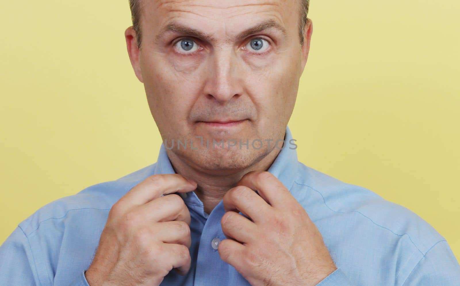 Close-up portrait of a handsome elderly man buttoning his blue shirt. A man in a blue shirt on a yellow background.