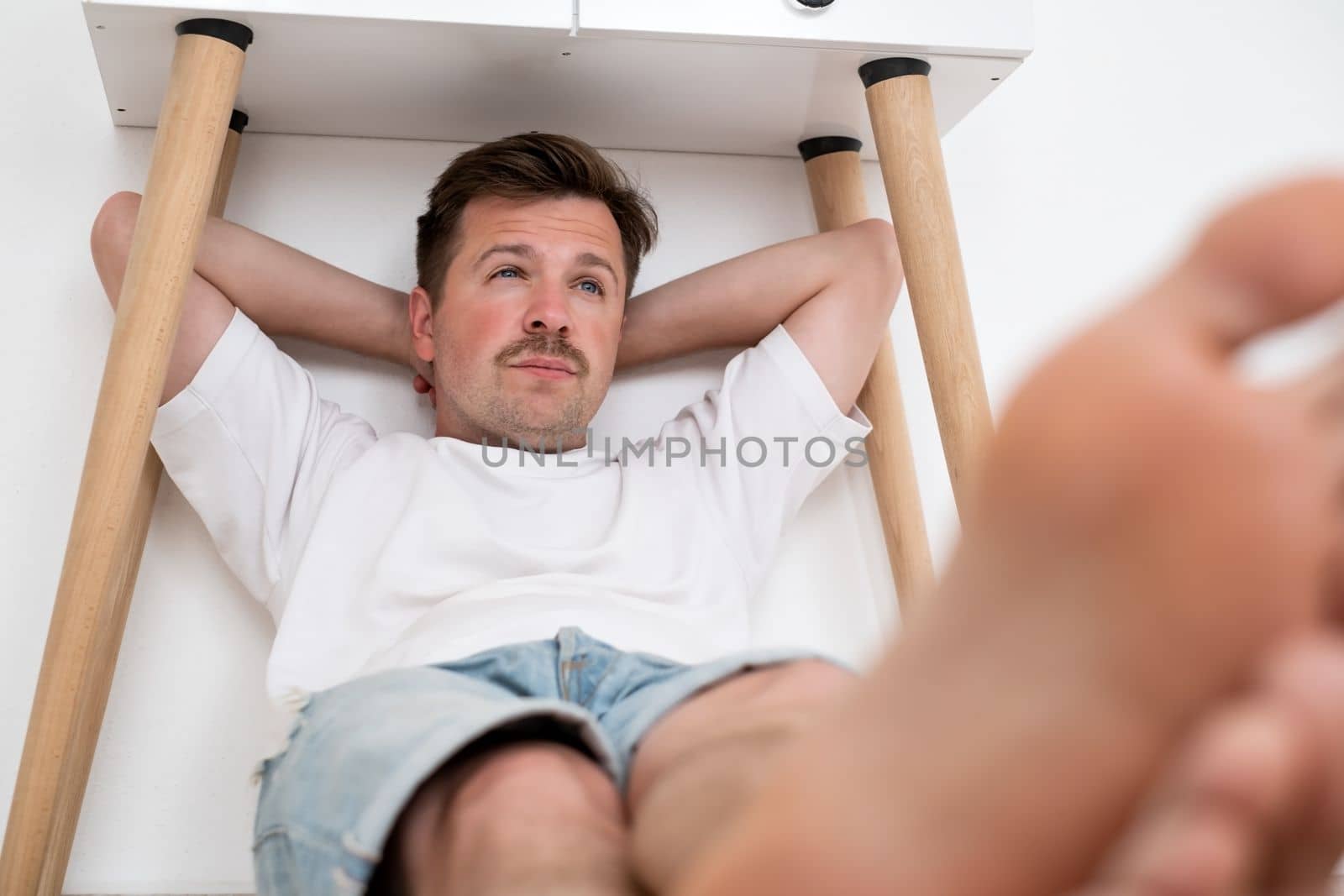 Scared man hiding under table in living room. Live me alone. Stress concept