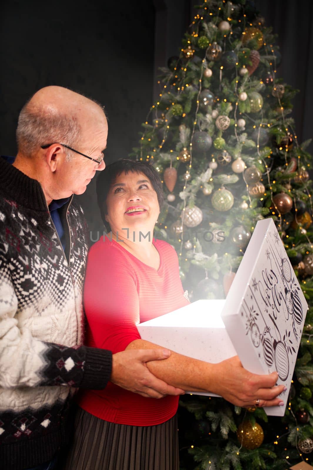 Man 60s giving a Christmas present to his woman. Opening gift box at christmas time. Christmas wonder concept by PhotoTime