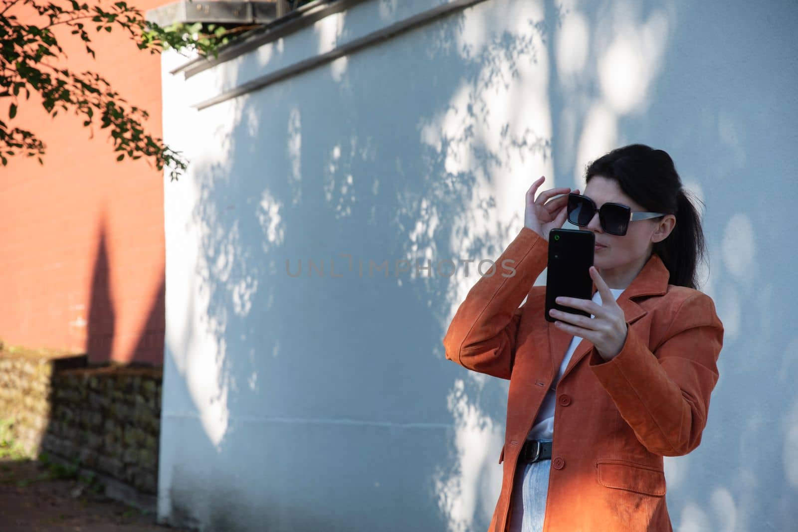 a young brunette girl in an orange jacket takes a selfie against the backdrop of a beautiful brick wall light and shadow contrast. High quality photo