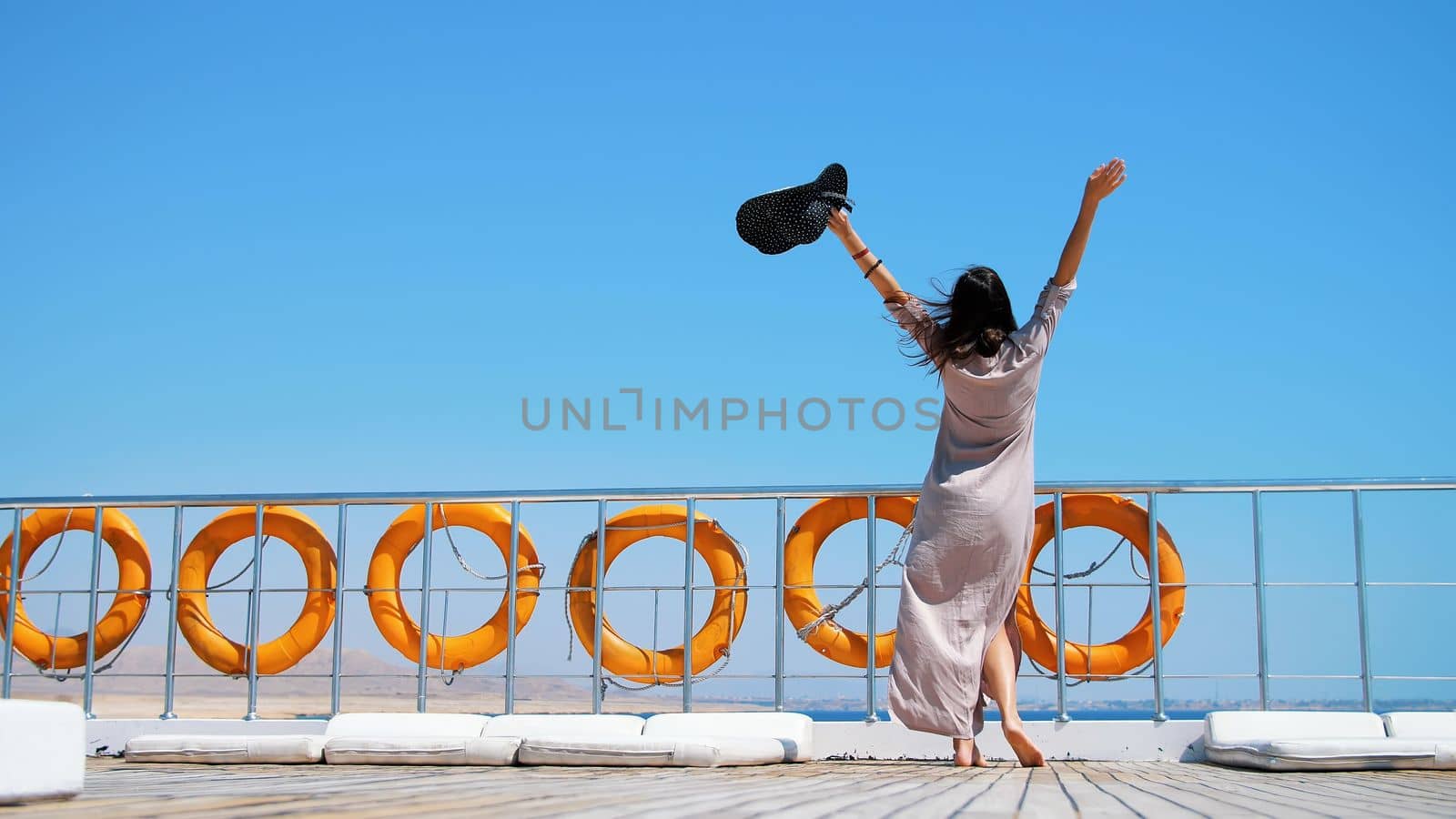 summer, sea, beautiful young brunette woman, in a long dress and sunglasses, stands on the deck of a ferry, ship, enjoying the rest, the beauty of the sea. on board hangs a lot of lifebuoys. High quality photo