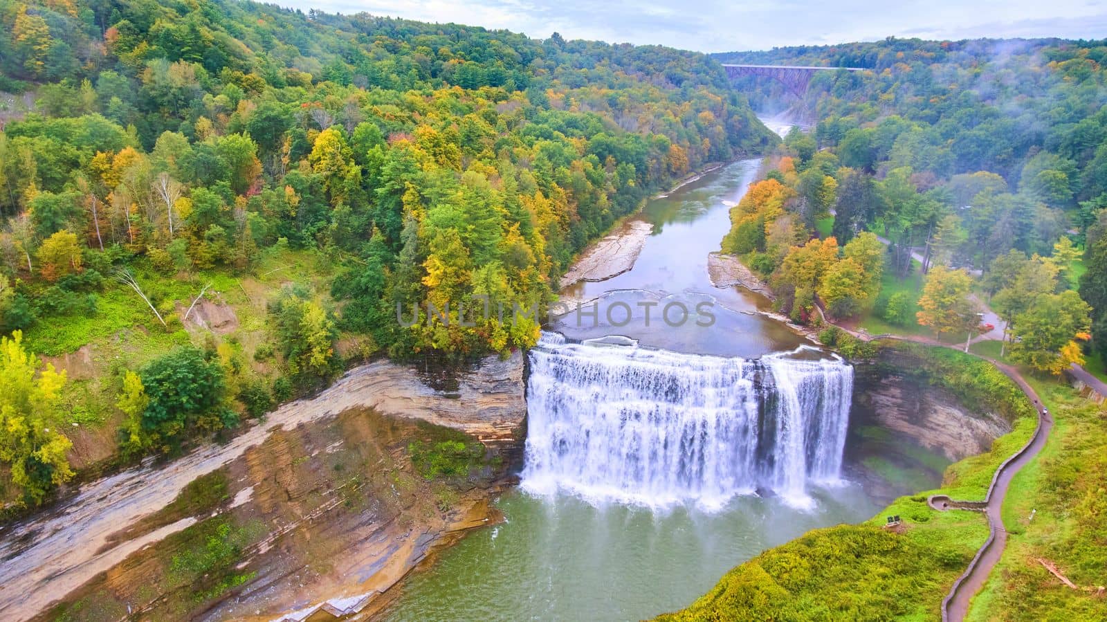Image of Aerial above huge waterfall in canyon during early fall with train track bridge in distance