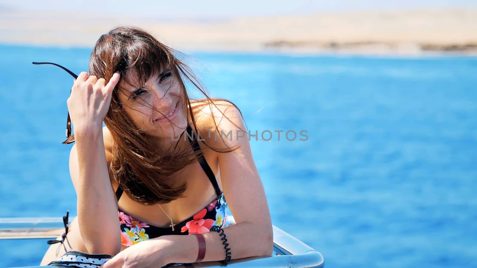 summer, sea, portrait, beautiful young brunette woman wearing a bathing suit and sunglasses, standing on the deck, enjoying the rest, her hair fluttering in the wind, happy,. High quality photo