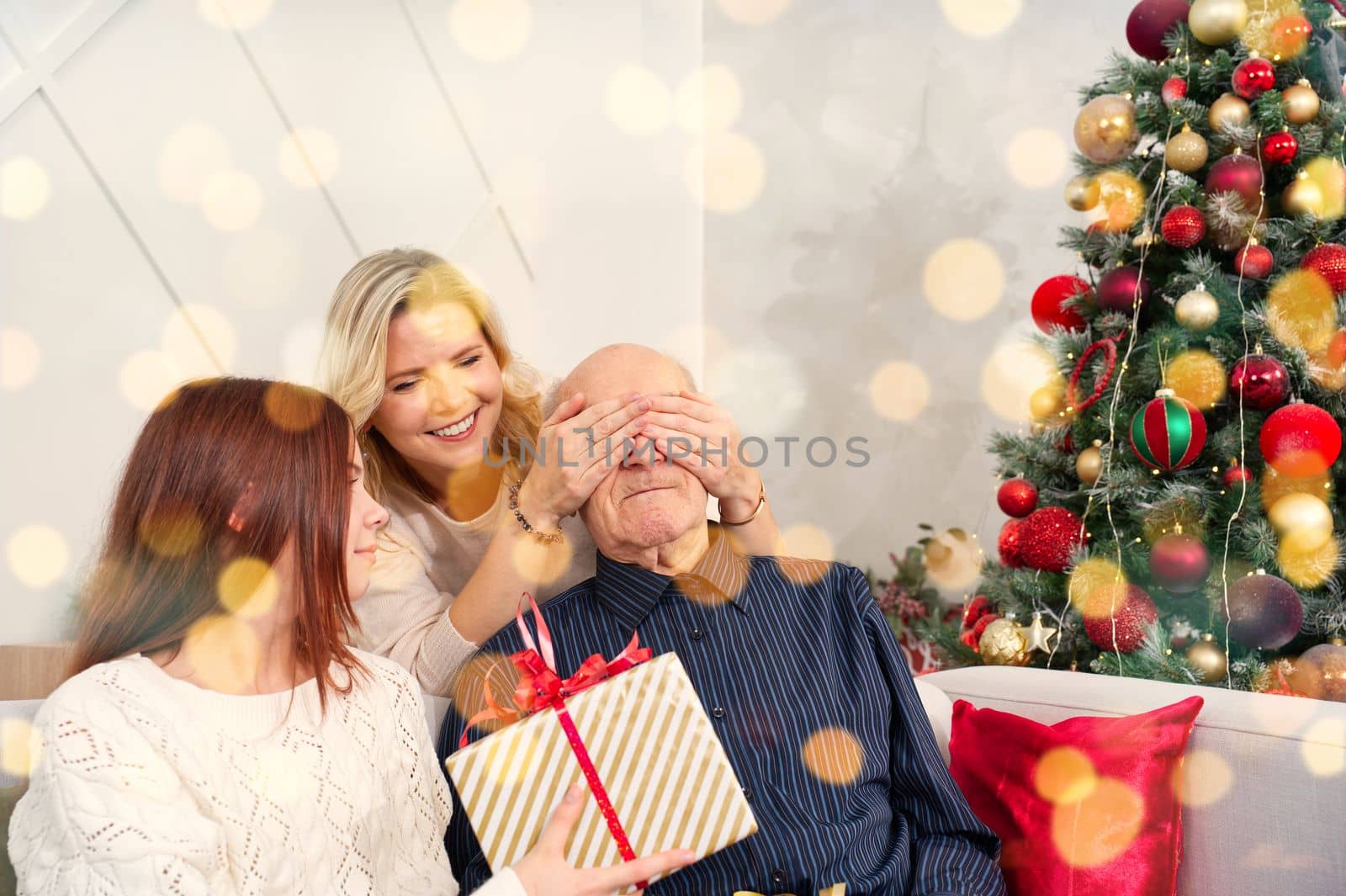 Granddaughters give a gift to grandfather. Happy senior man embracing his granddaughter while receiving a gift on Christmas at home. Happy family grandfather with cute excited granddaughter.