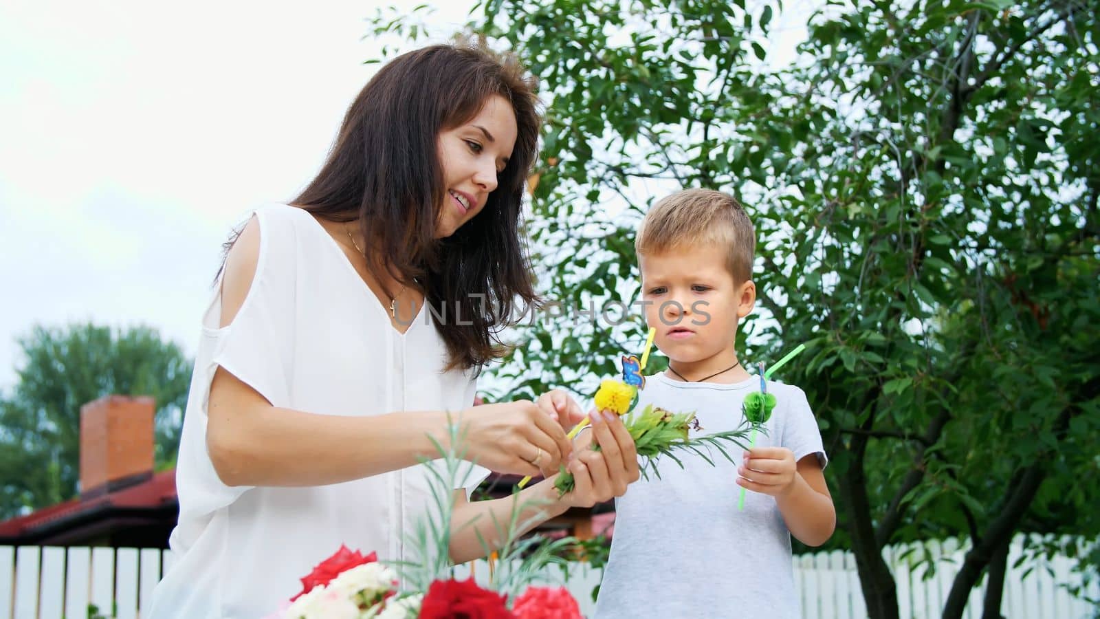 summer, in the garden, slow motion, Mom with a four-year-old son decorate the straw for juice. The boy likes it very much, he rejoices, has fun, shows his tongue. High quality photo