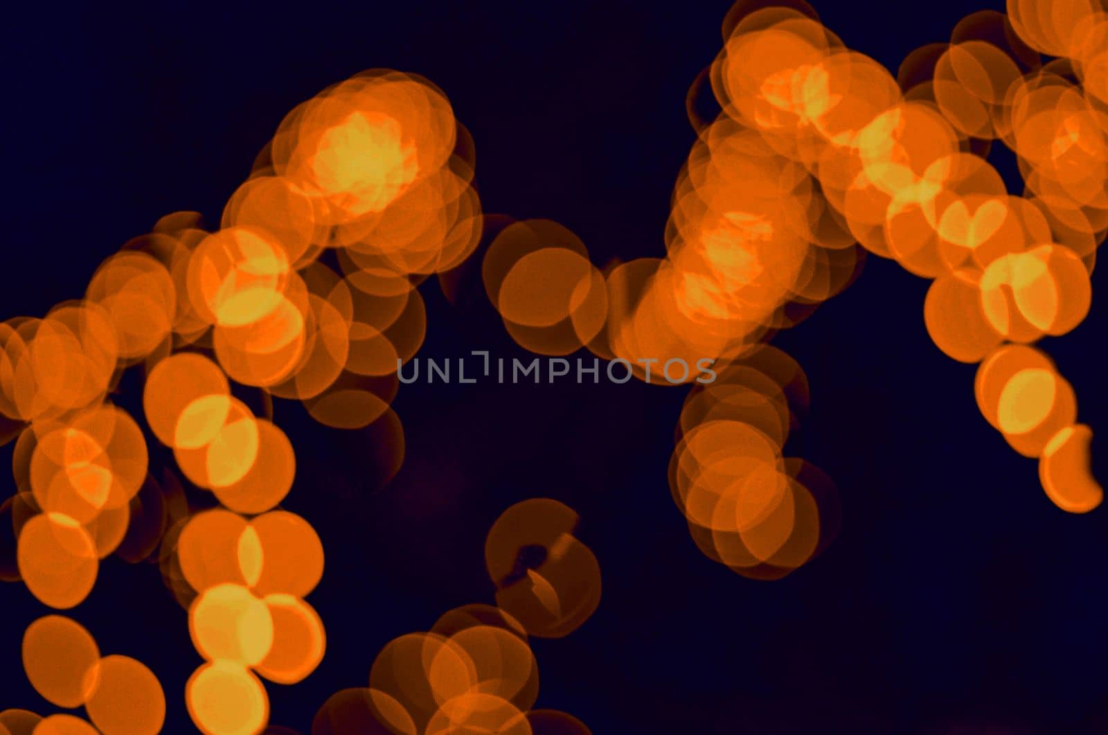 Enigmatic and romantic bokeh from blue glowing garlands. Festive new year lighting. Festive new year lighting Orange bokeh of electric garlands on a dark background.