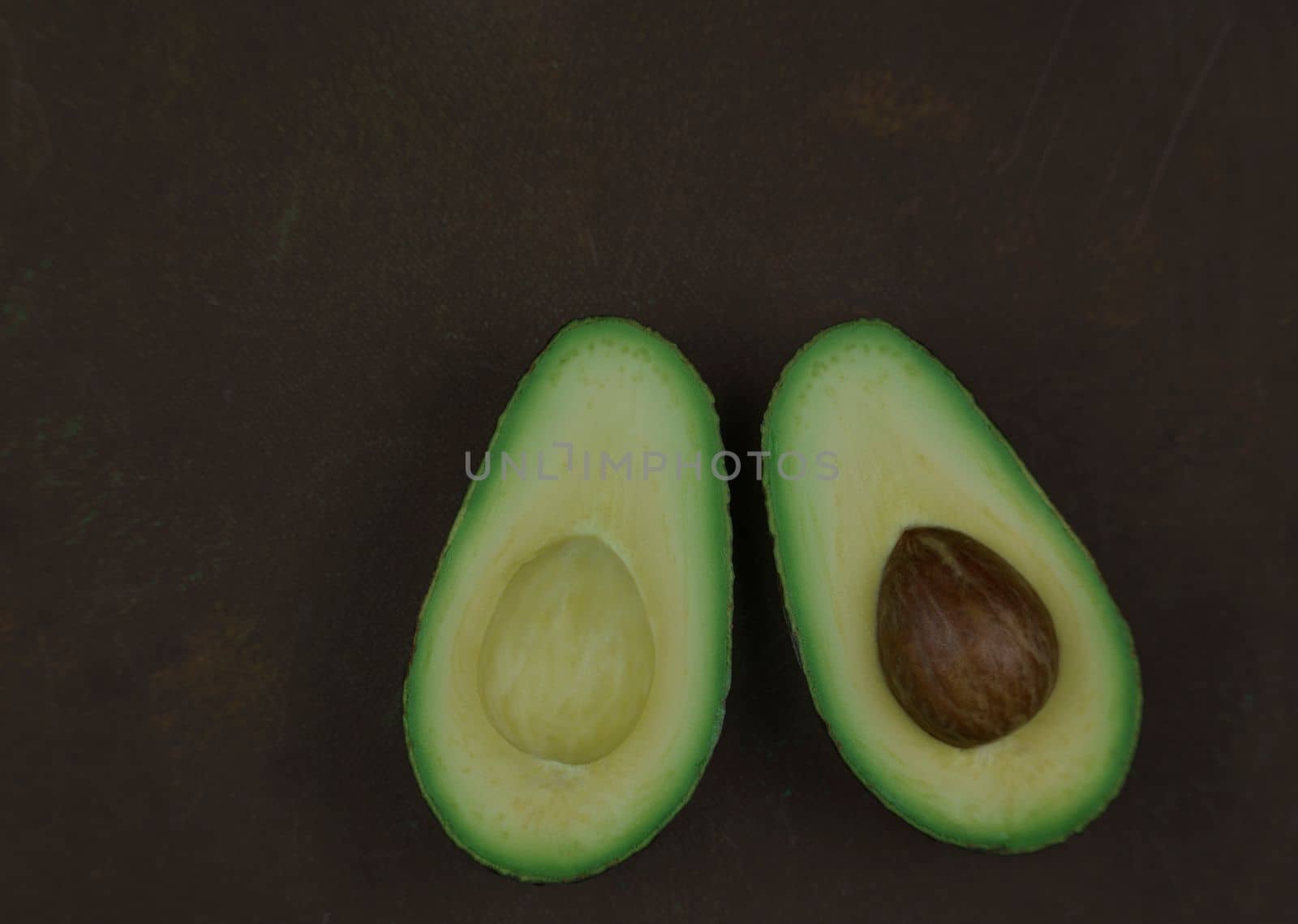 Avocado fruit two halfes on green background. Green avocado, minimal flat lay style with copy space. by Costin