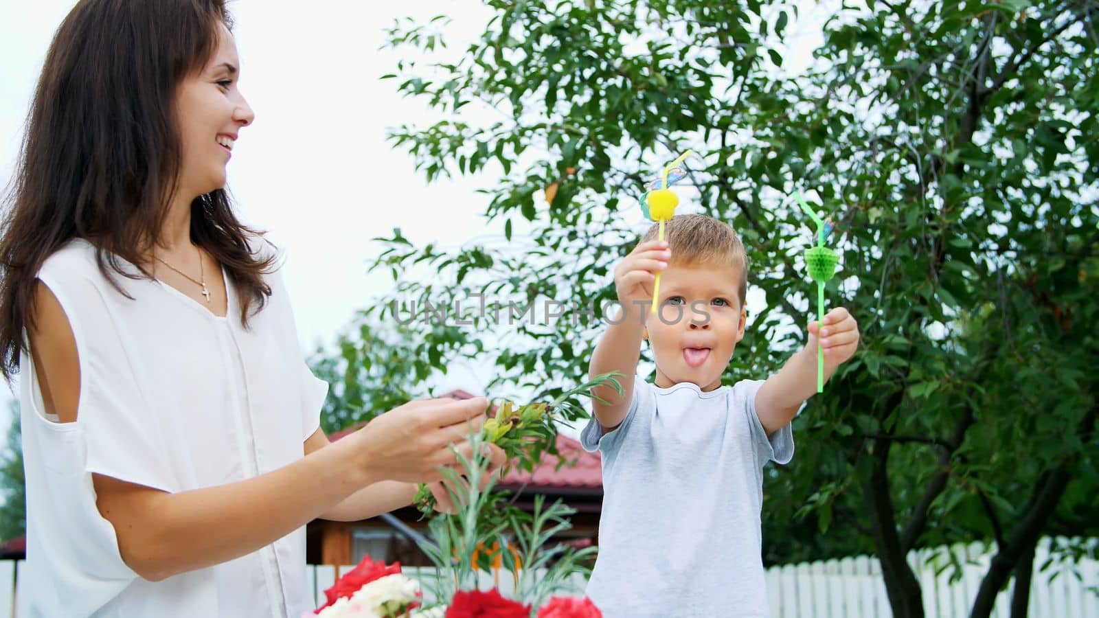 summer, in the garden, slow motion, Mom with a four-year-old son decorate the straw for juice. The boy likes it very much, he rejoices, has fun, shows his tongue. High quality photo