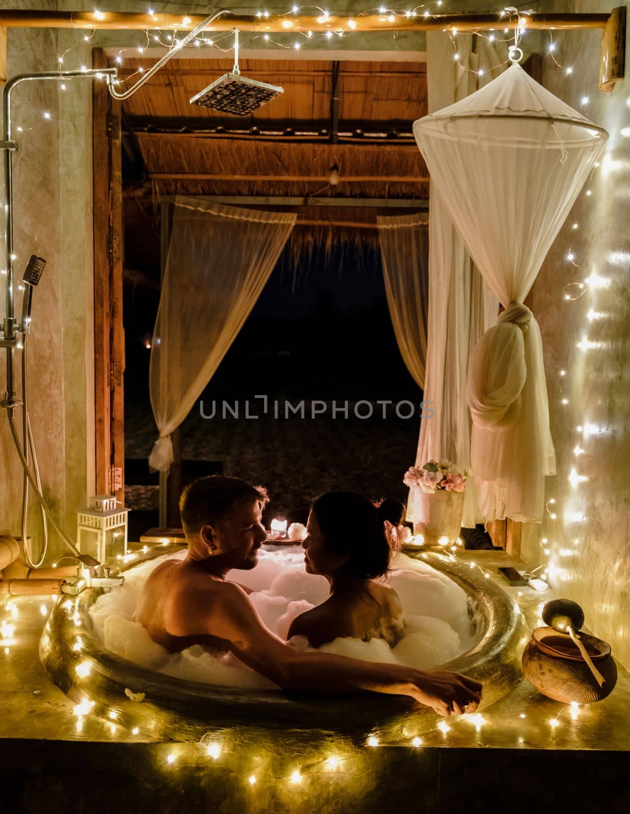 A couple of caucasian men and Asian women in a bathtub in the evening during sunset, a couple in a bathtub.