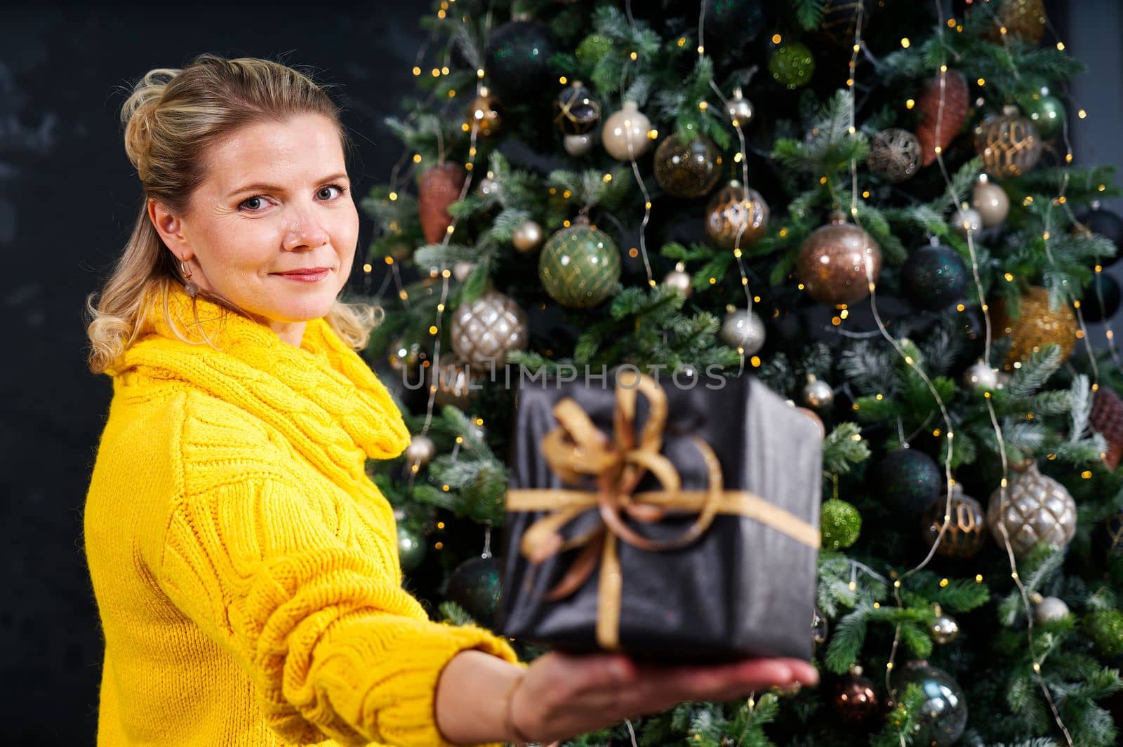 beautiful blonde woman holding a box with a christmas present in her hand. Decorated Christmas tree on background. by PhotoTime