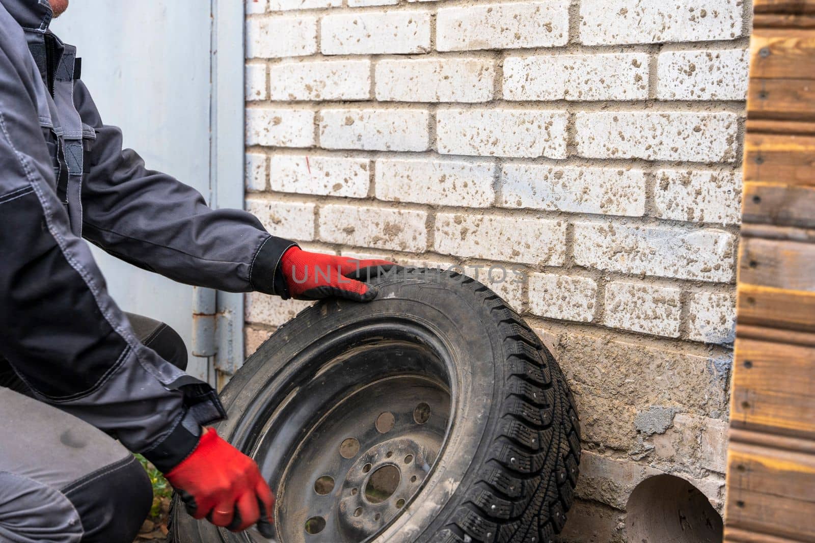 a male car mechanic in overalls inspects the wheel of a car. Car repair, seasonal replacement of car tires.