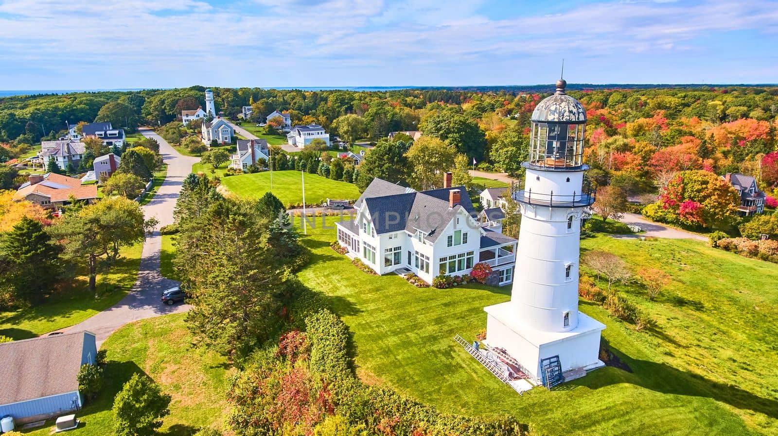 Homes and fall forest surround pair of Maine Lighthouses on ocean by njproductions