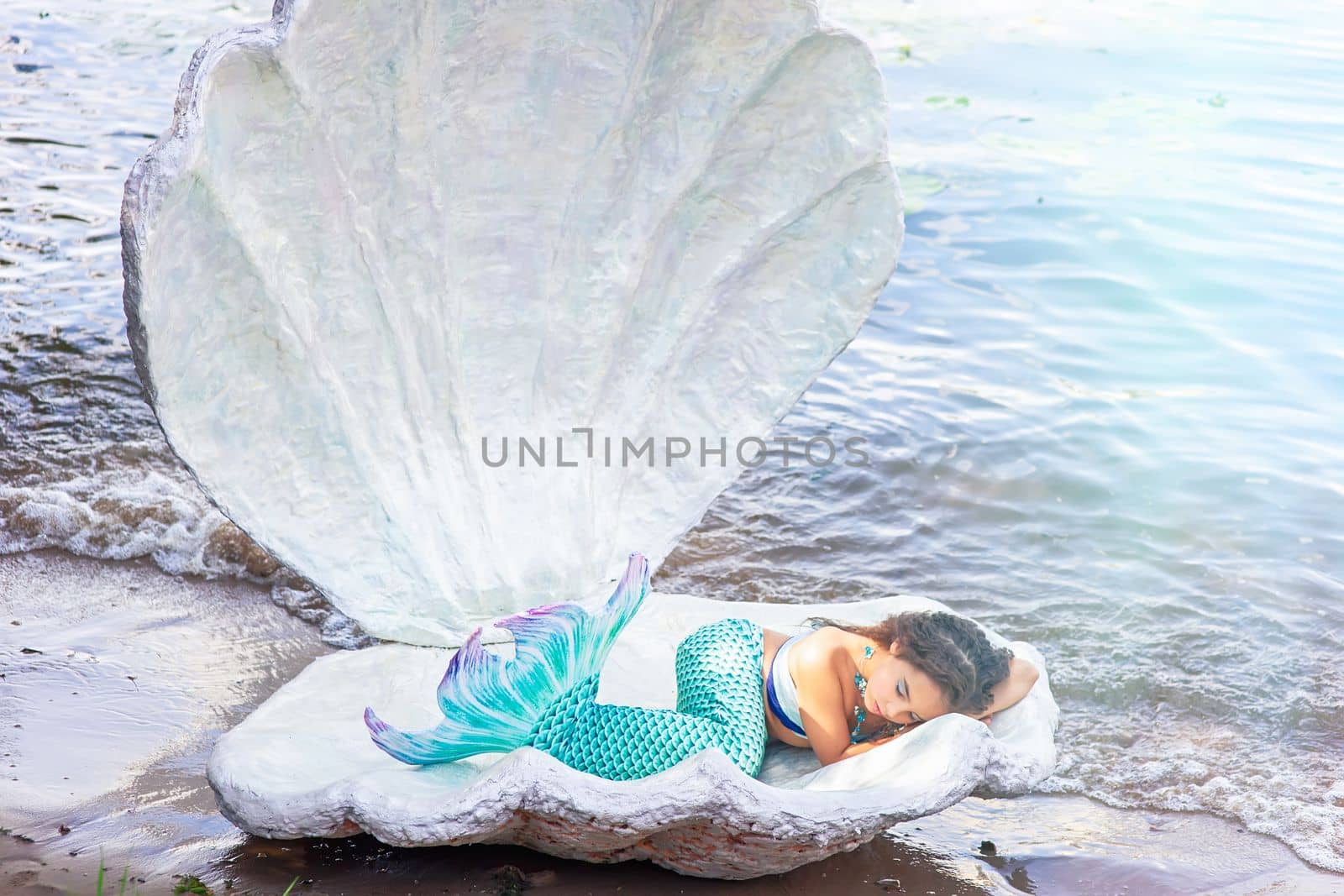 A pretty little girl in a turquoise mermaid costume sleeping in a large sea shell by Zakharova